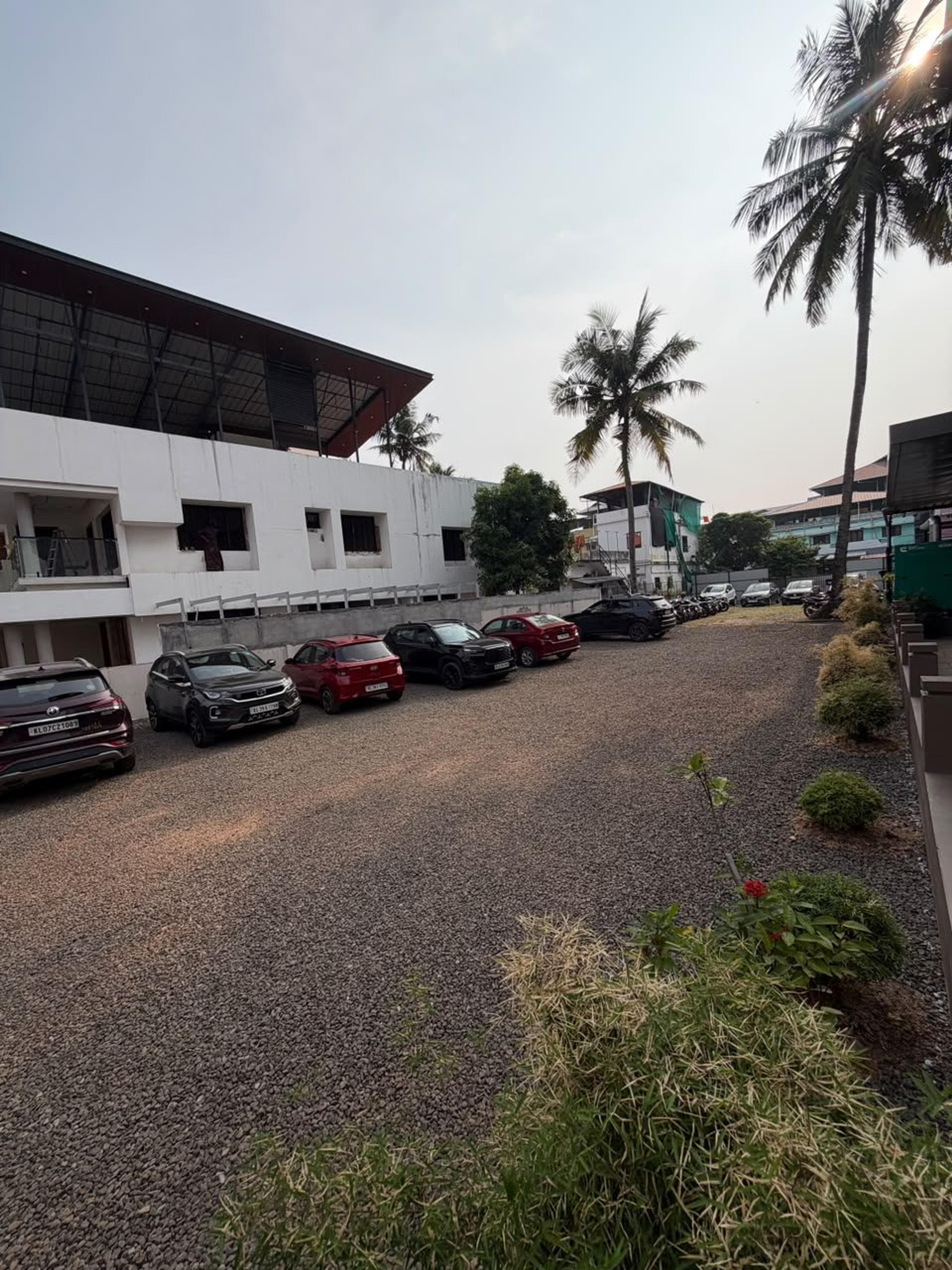 On-site car parking on gravel beside G K Tower, lined with plants and coconut palms