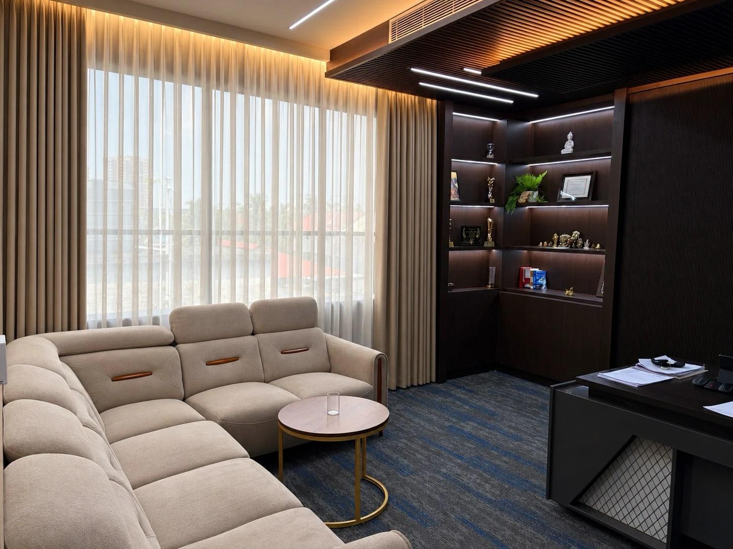 Luxury cabin with a corner sofa, sheer curtains over a large window, lit display shelves and an executive desk