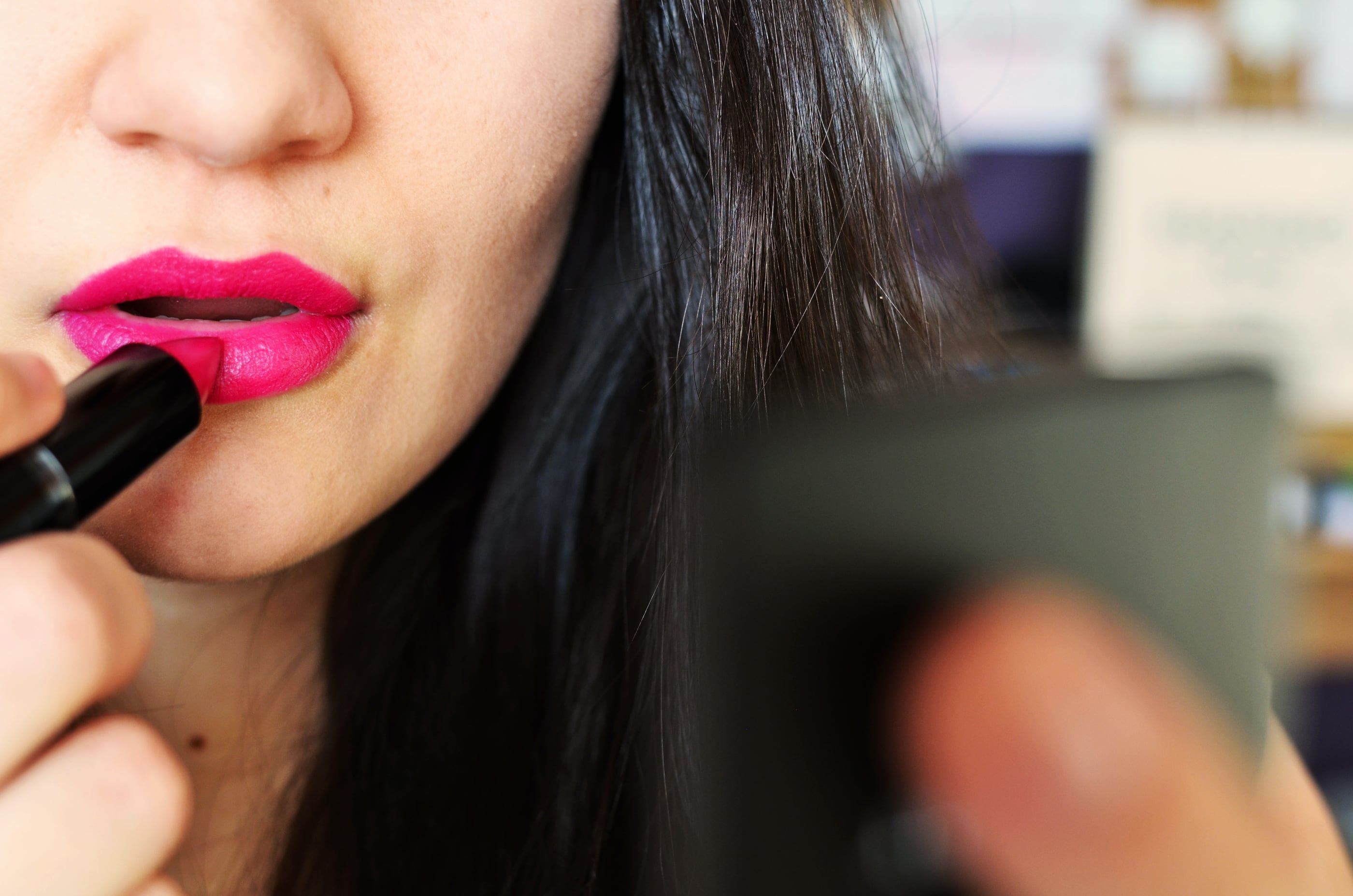 Close-up of a woman applying bright pink lipstick