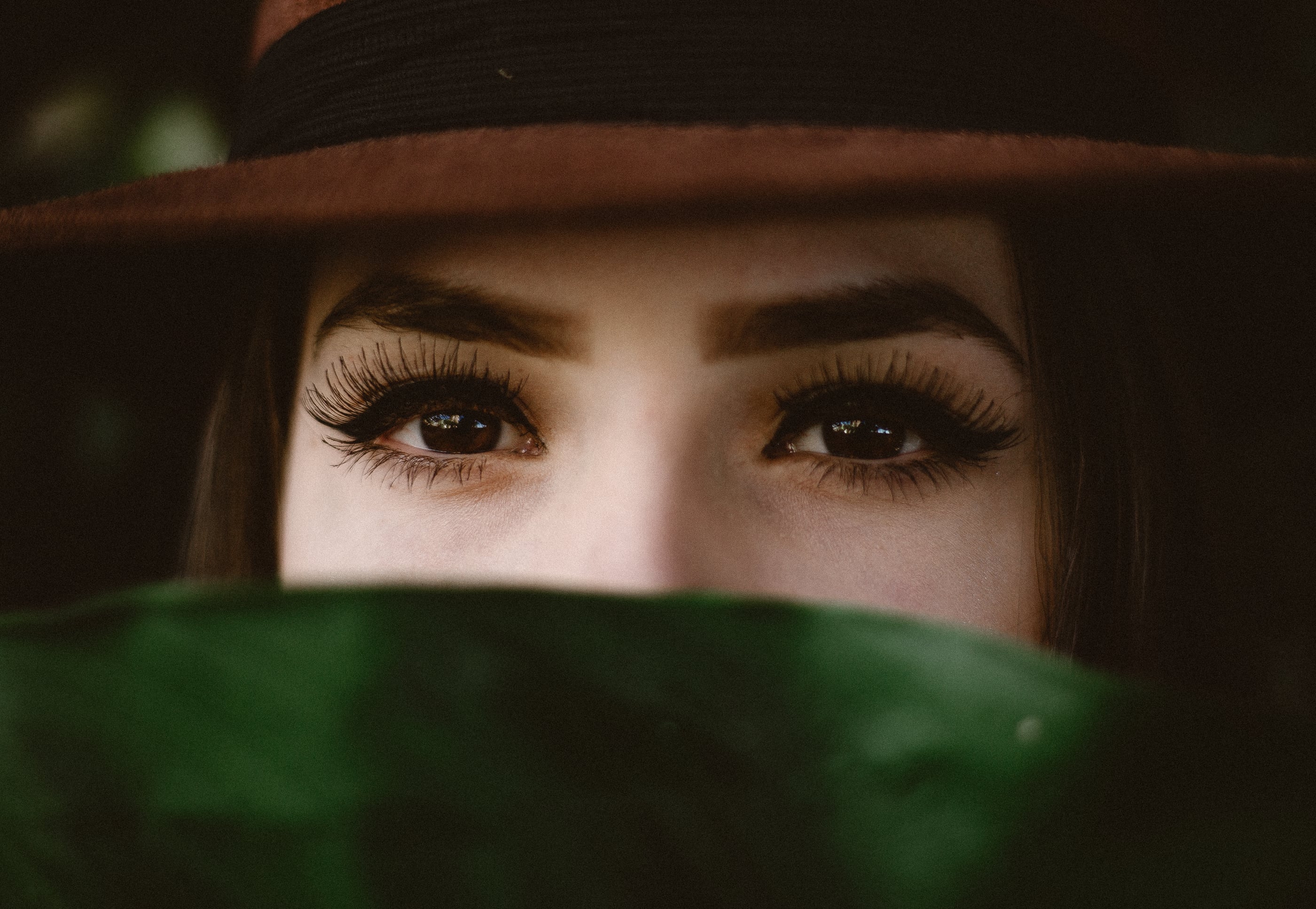 A close-up of a woman's eyes with dramatic lashes, beneath the brim of a hat