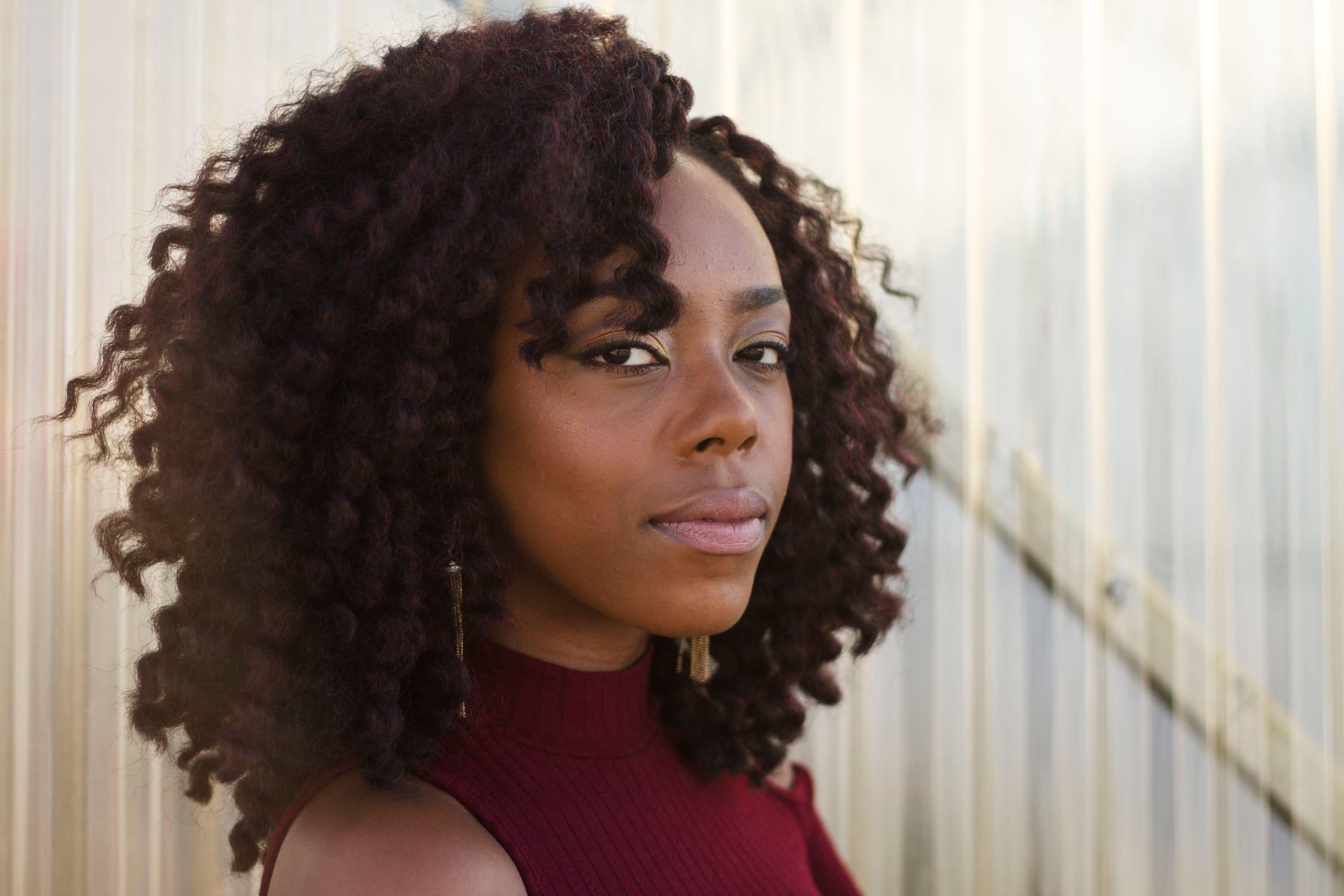 Portrait of a woman with natural curls and a deep red top, looking at the camera