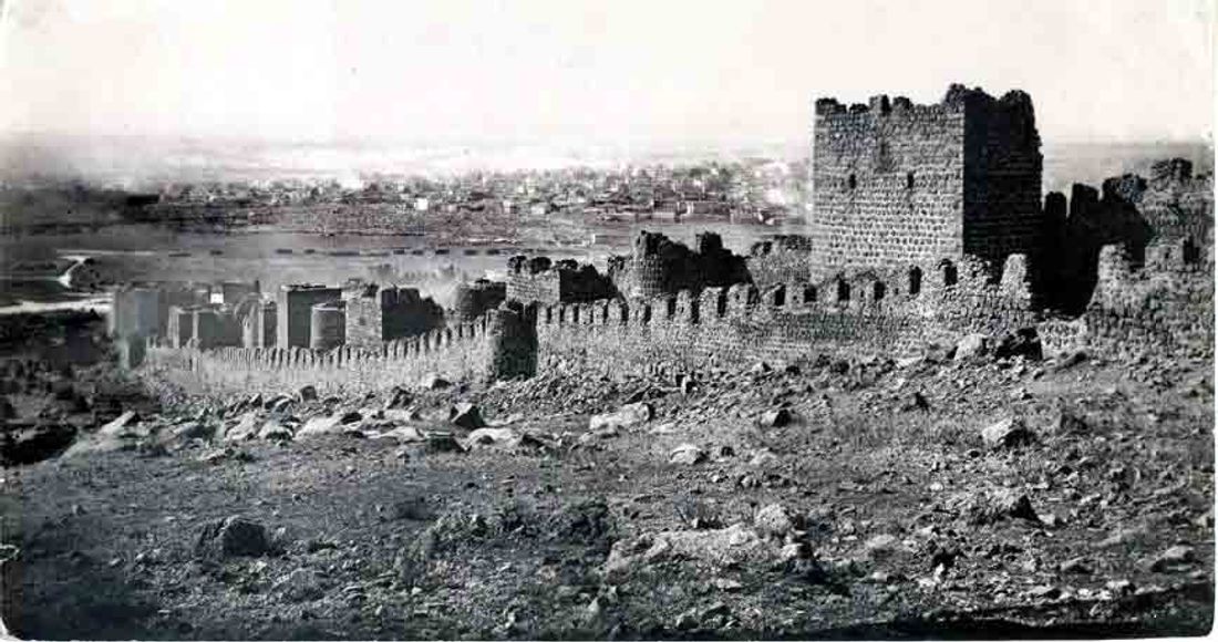 Tarihi kale ve şehir manzarası. Taş yapıların silüeti ve şehir arkada beliriyor.