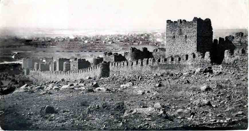 Tarihi kale ve şehir manzarası. Taş yapıların silüeti ve şehir arkada beliriyor.
