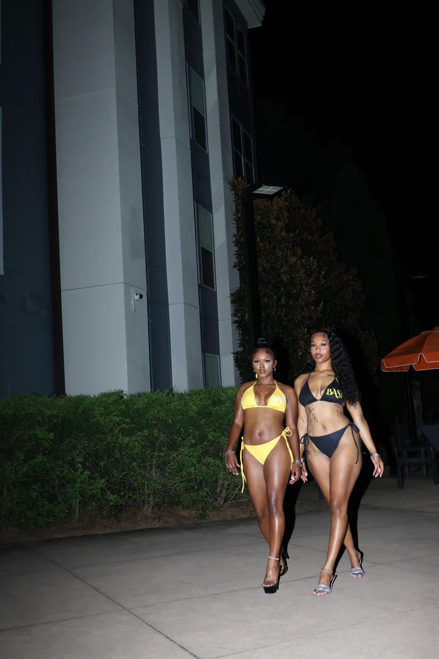 Two women wearing yellow and black string bikinis walking at night