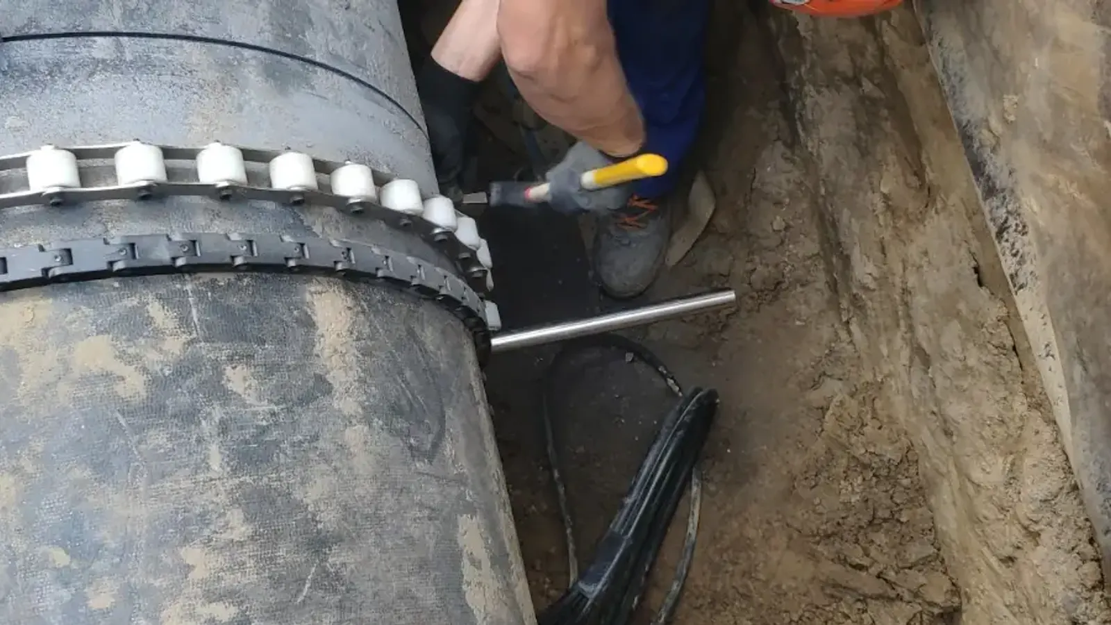 Operator w kasku prowadzi piłę obwodową po rurze w wykopie