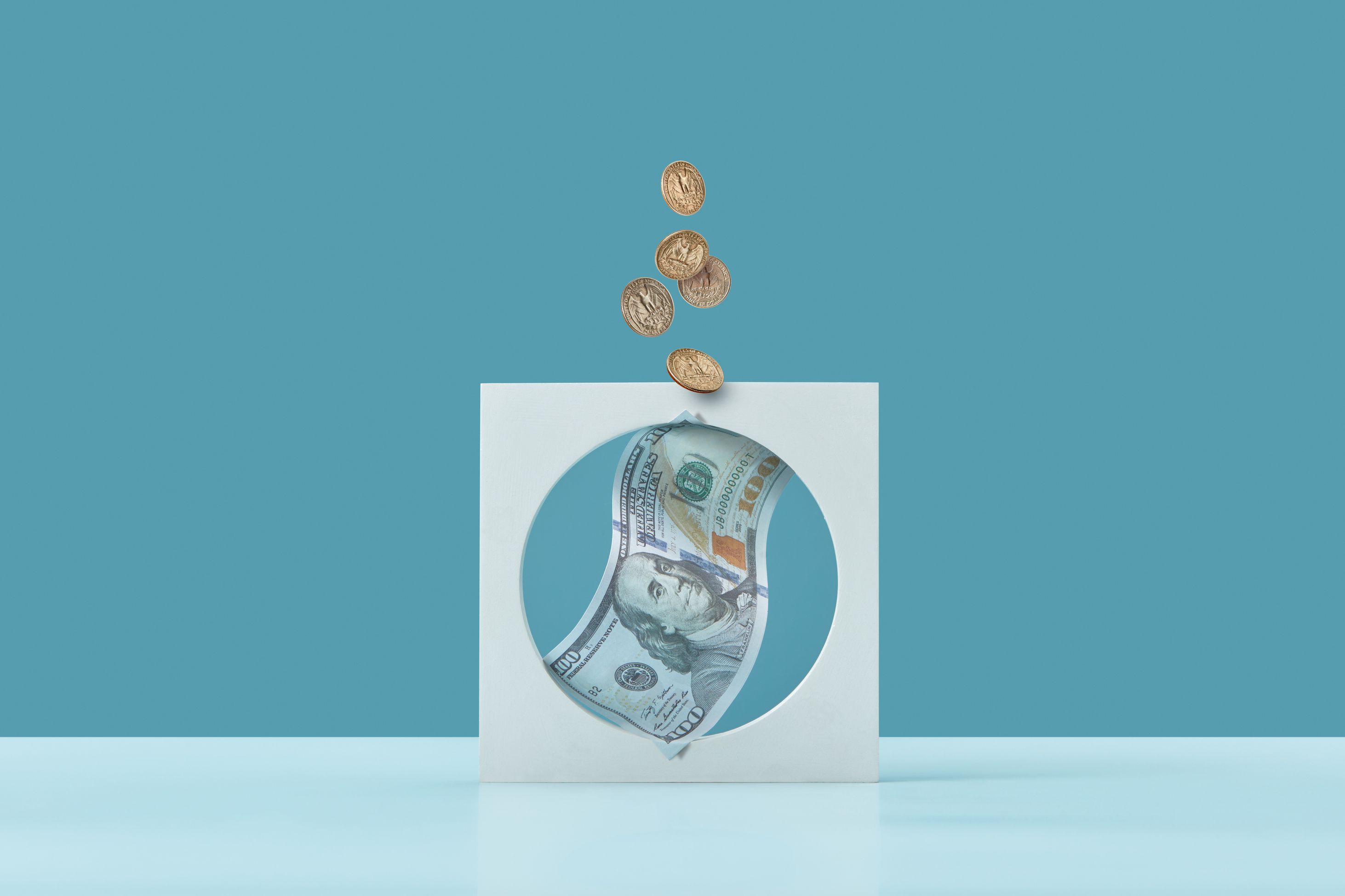 An image of a 100 dollar bill in a circle with coins falling down on it on a sky blue background. 