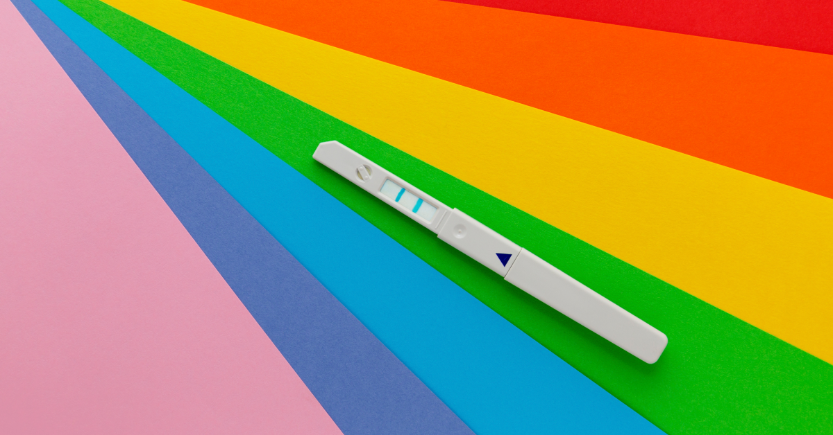 A pregnancy test against a rainbow colored background. 