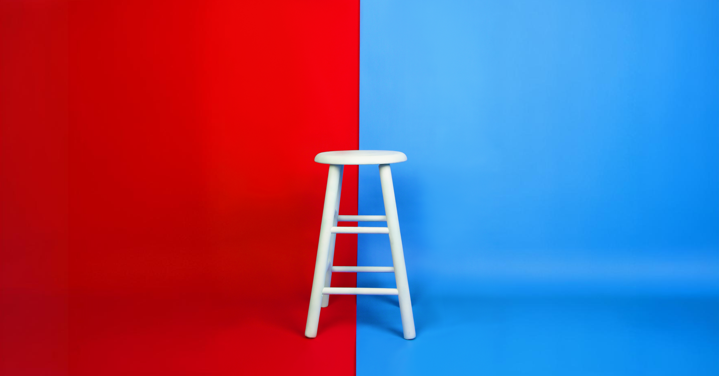 A white stool against a split blue and red background. 