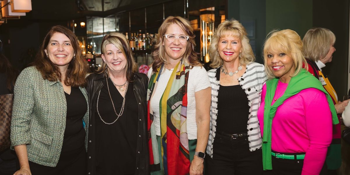 Five members standing together and smiling, while posing for the camera
