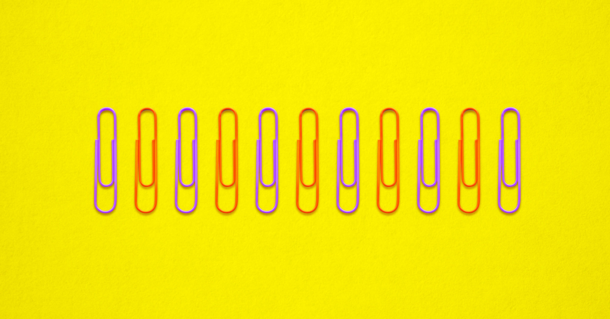 A straight line of purple and red paper clips on a yellow background. 