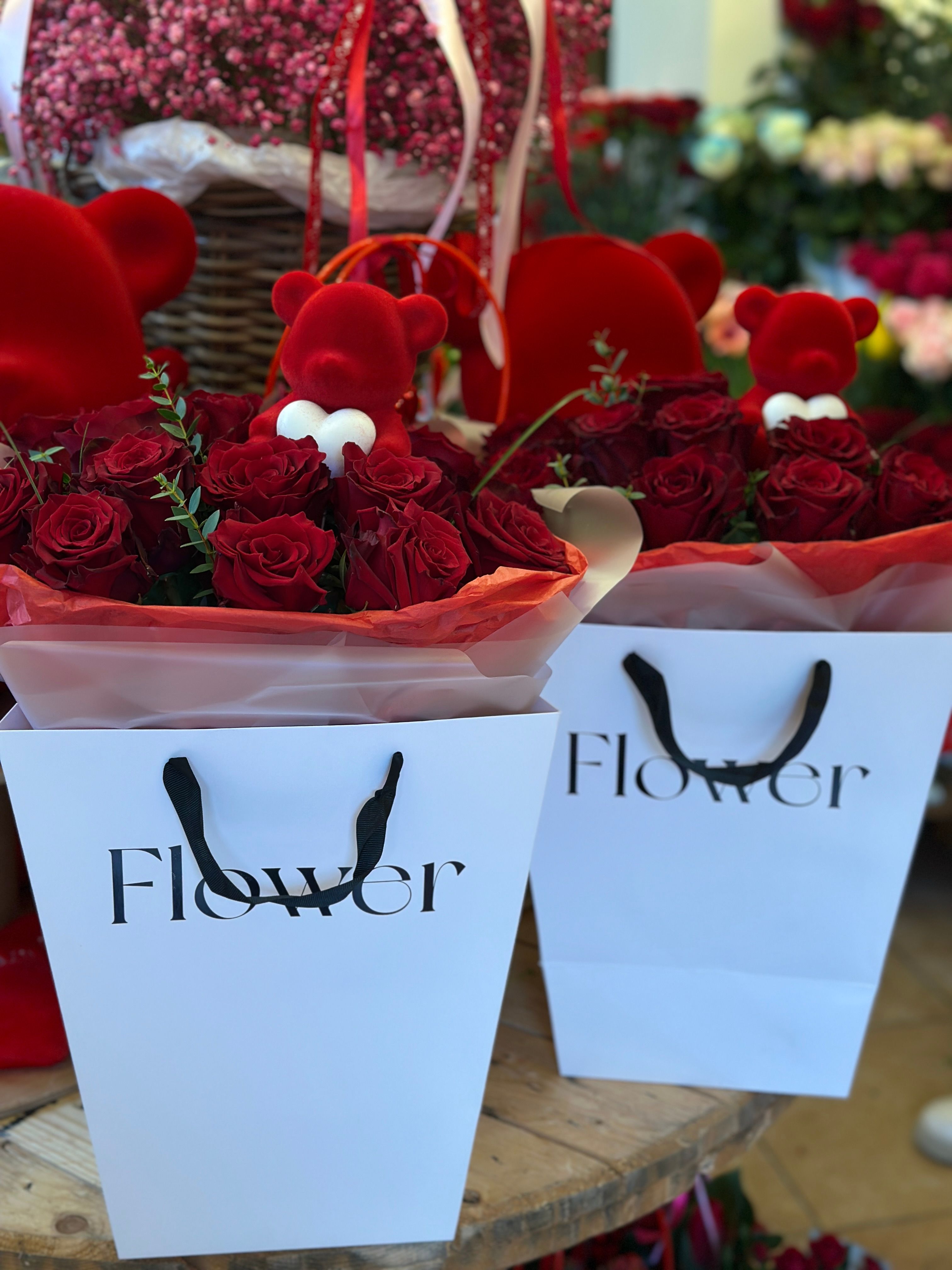 Flowerbox w eleganckiej białej torbie, wypełniony świeżymi czerwonymi różami i ozdobiony uroczym czerwonym misiem.