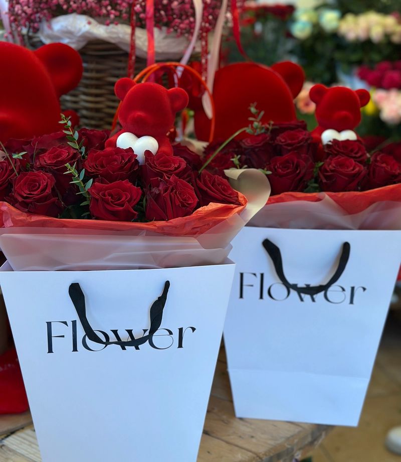 Flowerbox w eleganckiej białej torbie, wypełniony świeżymi czerwonymi różami i ozdobiony uroczym czerwonym misiem.