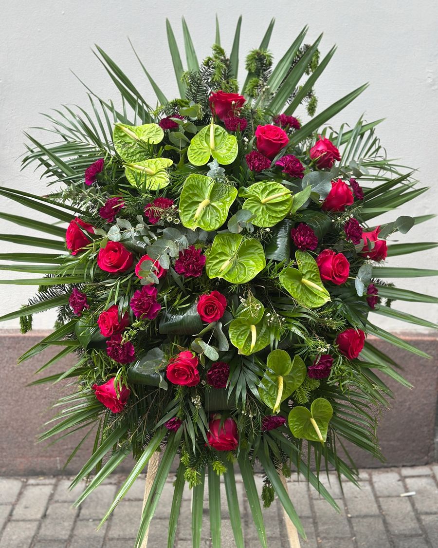 Wieniec pogrzebowy w kształcie łezki z czerwonych róż, zielonego anturium oraz fioletowych goździków.
