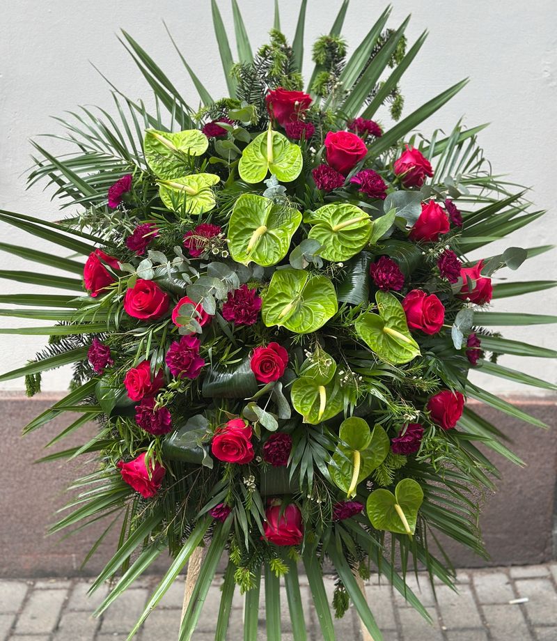 Wieniec pogrzebowy w kształcie łezki z czerwonych róż, zielonego anturium oraz fioletowych goździków.