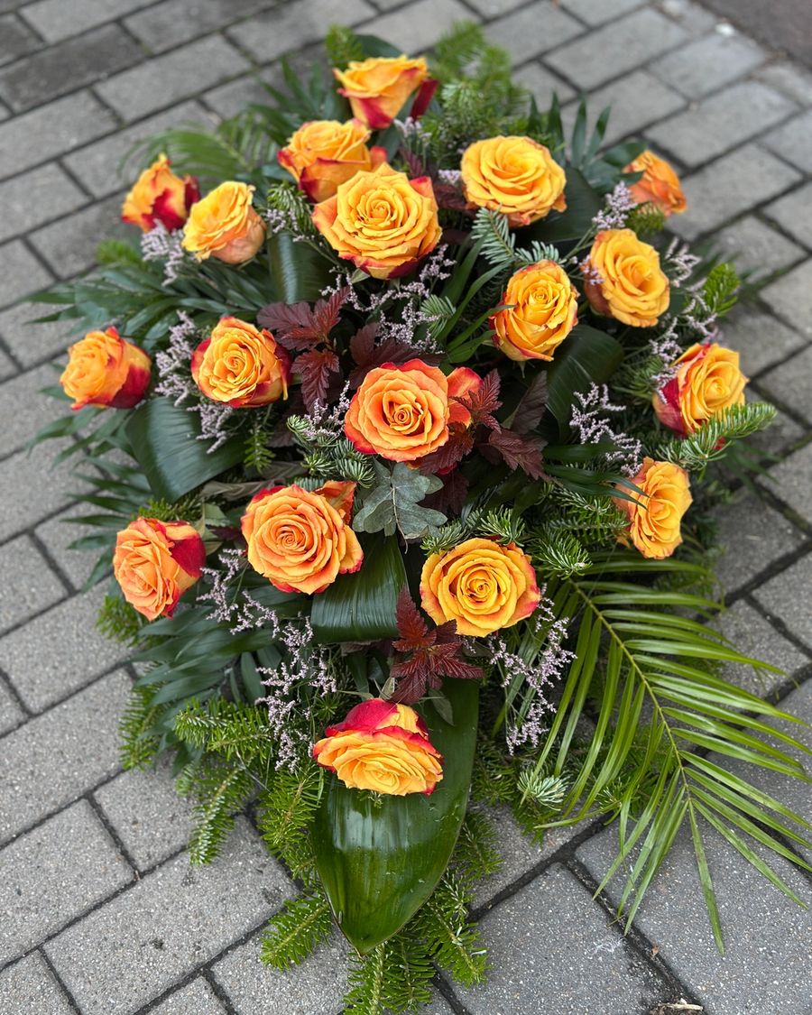 Wiązanka pogrzebowa w kształcie łezki z róż herbacianych, uzupełniona zielonymi dodatkami florystycznymi, ułożona na podkładzie z jodły i florecie z dostępem do wody.