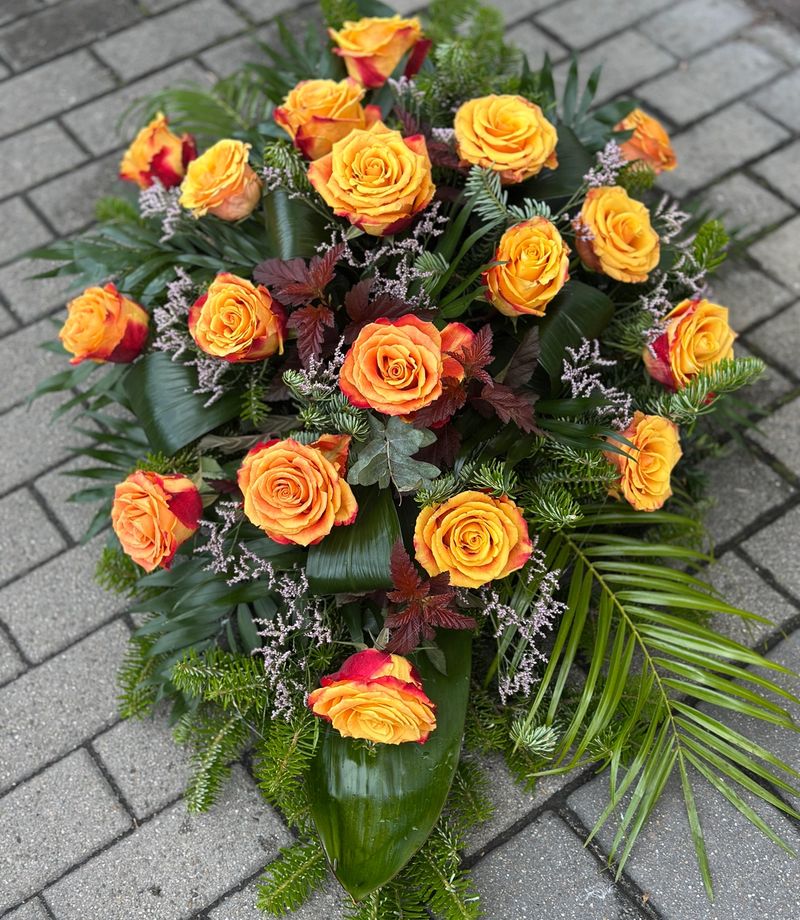 Wiązanka pogrzebowa w kształcie łezki z róż herbacianych, uzupełniona zielonymi dodatkami florystycznymi, ułożona na podkładzie z jodły i florecie z dostępem do wody.
