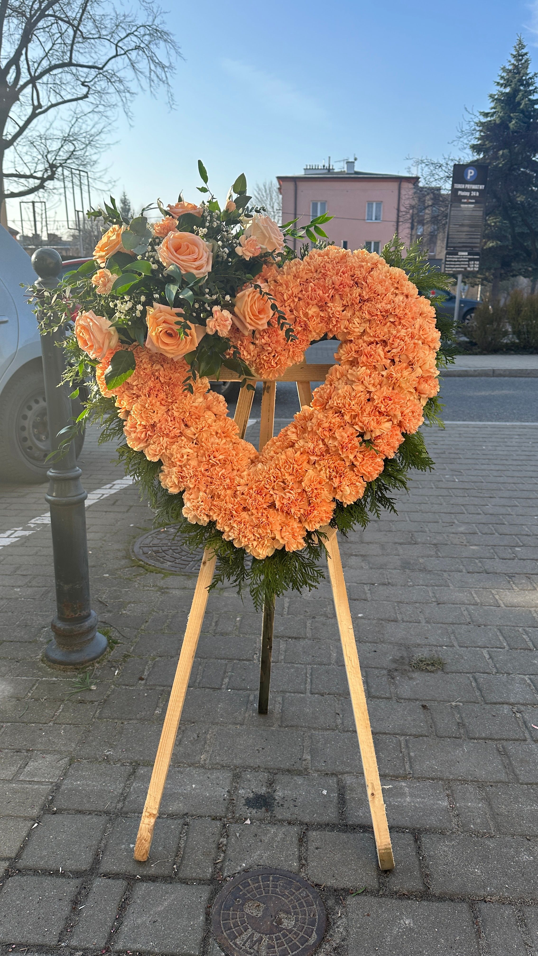 Wieniec w kształcie serca na trzech nogach z pomarańczowych goździków i róż.