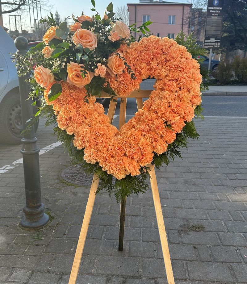 Wieniec w kształcie serca na trzech nogach z pomarańczowych goździków i róż.