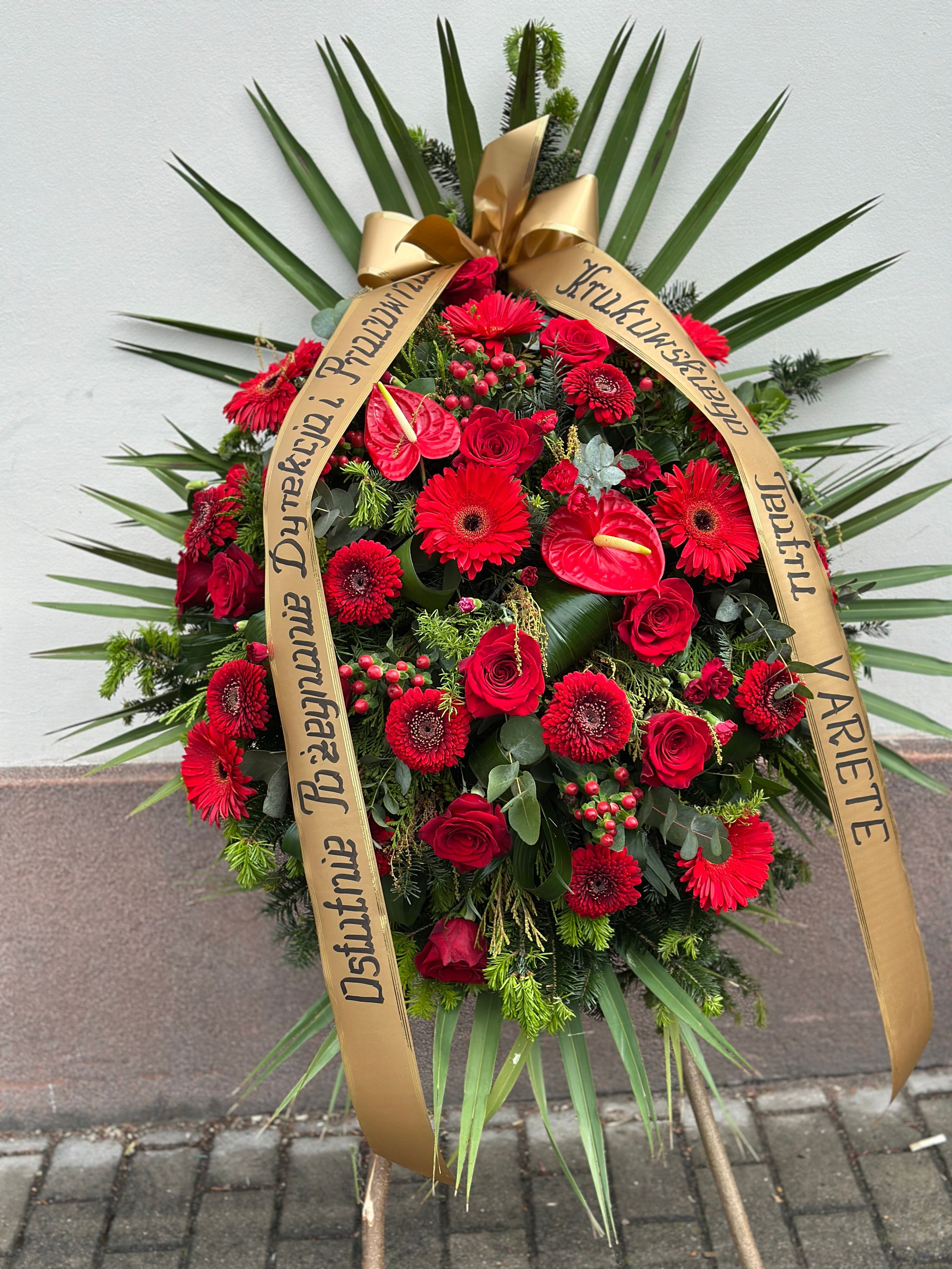 Wieniec klasyczny łezka w odcieniach czerwieni i bordo, uzupełniony różnorodnymi kwiatami, między innymi anturium, różą, gerberą oraz goździkiem.