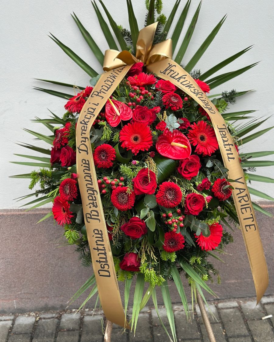 Wieniec klasyczny łezka w odcieniach czerwieni i bordo, uzupełniony różnorodnymi kwiatami, między innymi anturium, różą, gerberą oraz goździkiem.