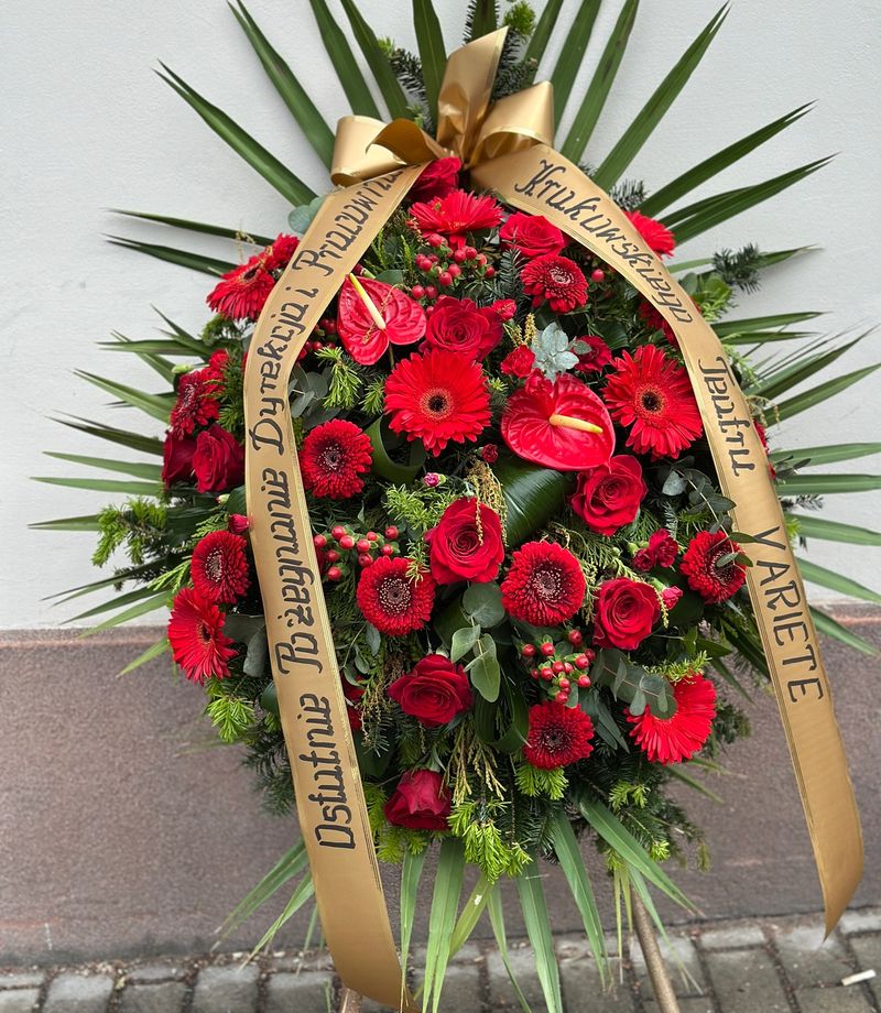 Wieniec klasyczny łezka w odcieniach czerwieni i bordo, uzupełniony różnorodnymi kwiatami, między innymi anturium, różą, gerberą oraz goździkiem.