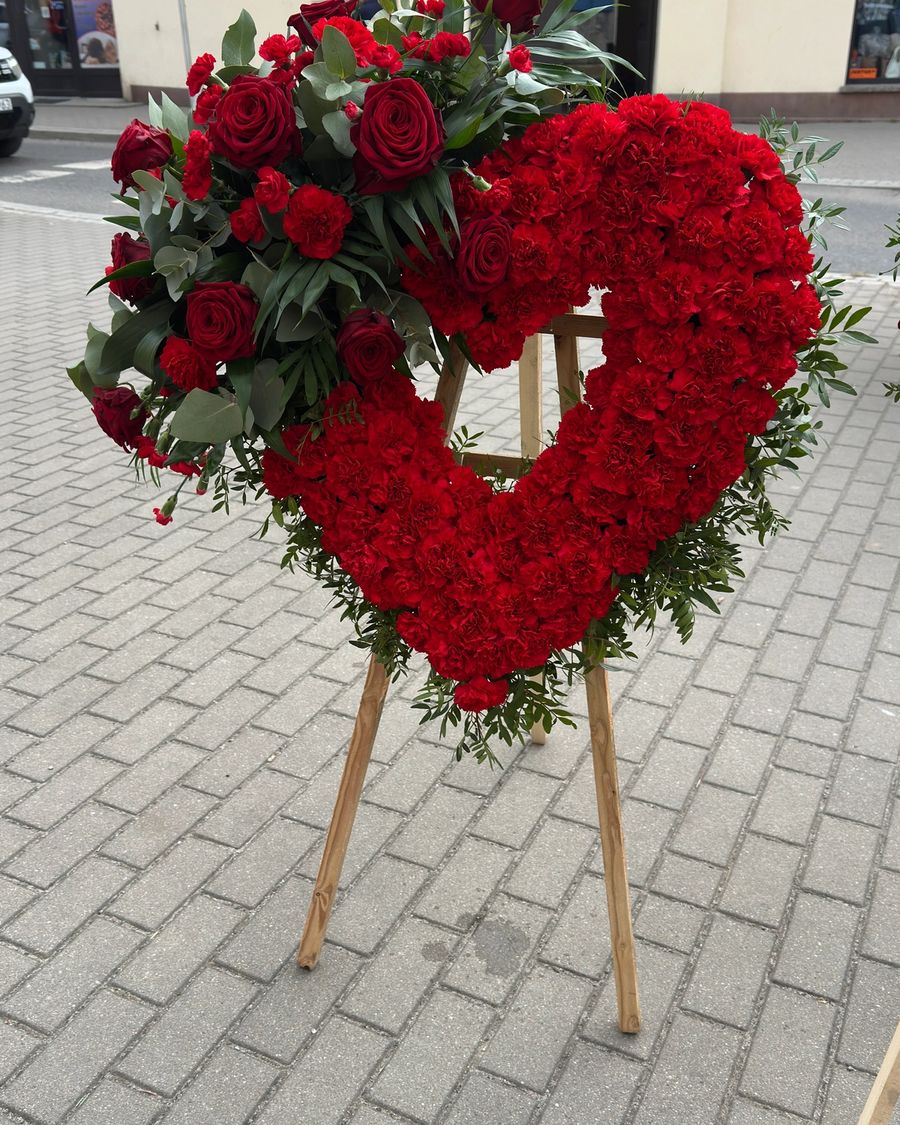Wieniec w kształcie serca na trzech nogach wykonany z czerwonych goździków i róż.