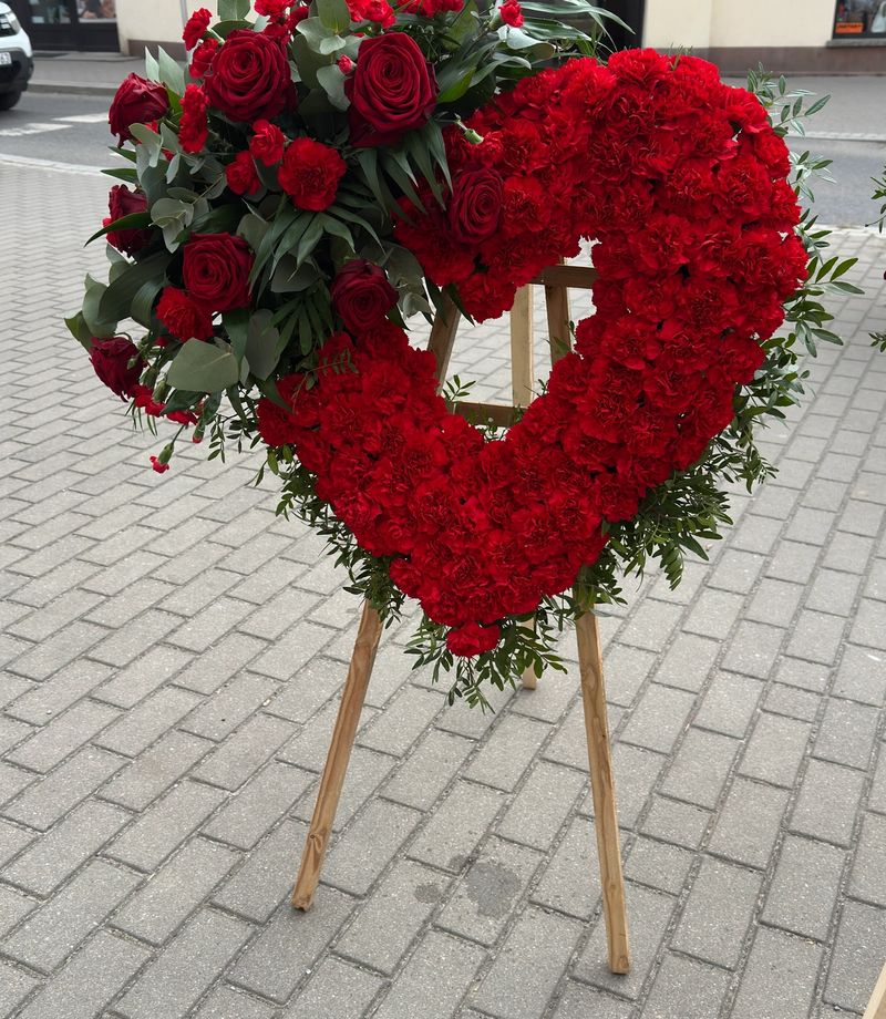 Wieniec w kształcie serca na trzech nogach wykonany z czerwonych goździków i róż.