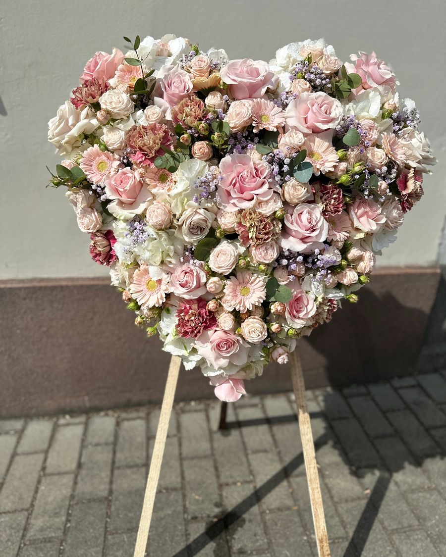 Wieniec pogrzebowy w kształcie serca, wykonany z różnorodnych kwiatów w delikatnych odcieniach pudrowego różu.