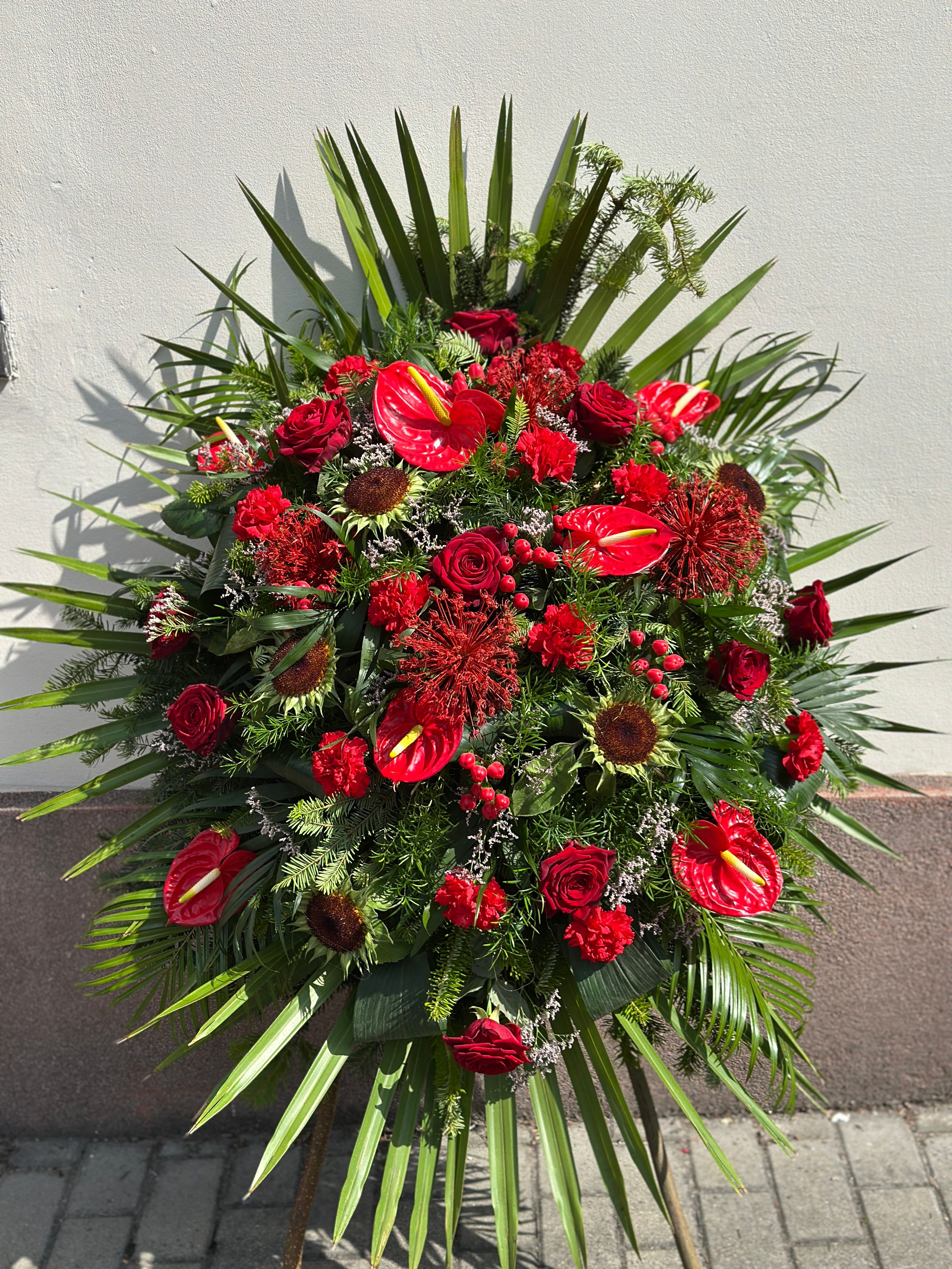 Wieniec pogrzebowy w kształcie łezki z czerwonych kwiatów. Mocna, klasyczna czerwień, wykonany z różnorodnych kwiatów w odcieniach bordo, tworzących dostojną i pełną głębi kompozycję