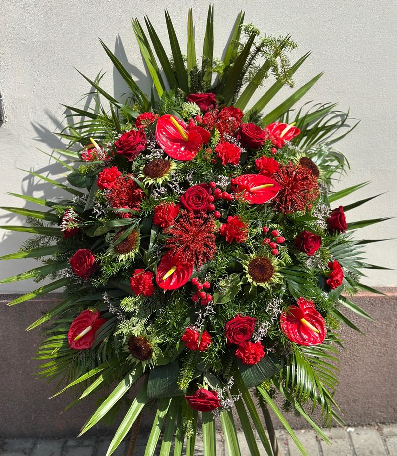 Wieniec pogrzebowy w kształcie łezki z czerwonych kwiatów. Mocna, klasyczna czerwień, wykonany z różnorodnych kwiatów w odcieniach bordo, tworzących dostojną i pełną głębi kompozycję