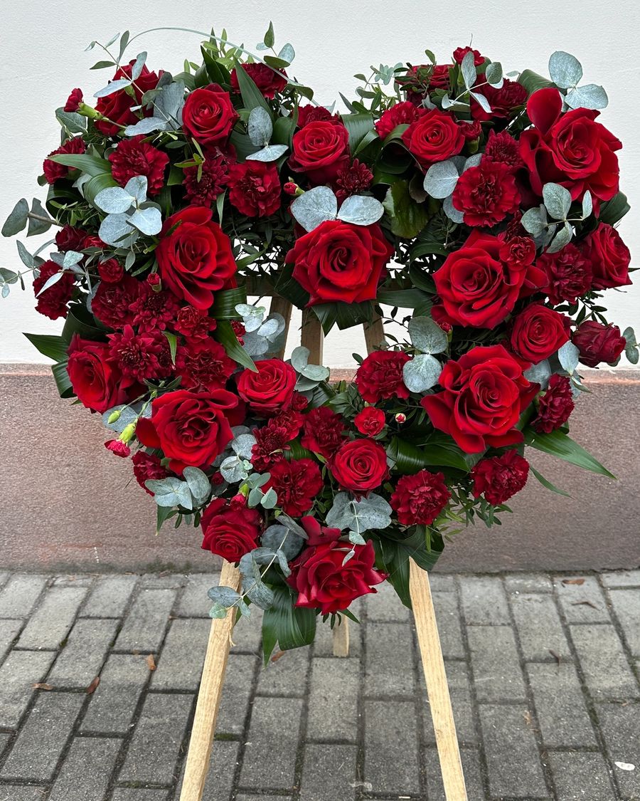 Wieniec pogrzebowy w kształcie serca na trzech nogach wykonany z czerwonych róż, goździka i eukaliptusa.