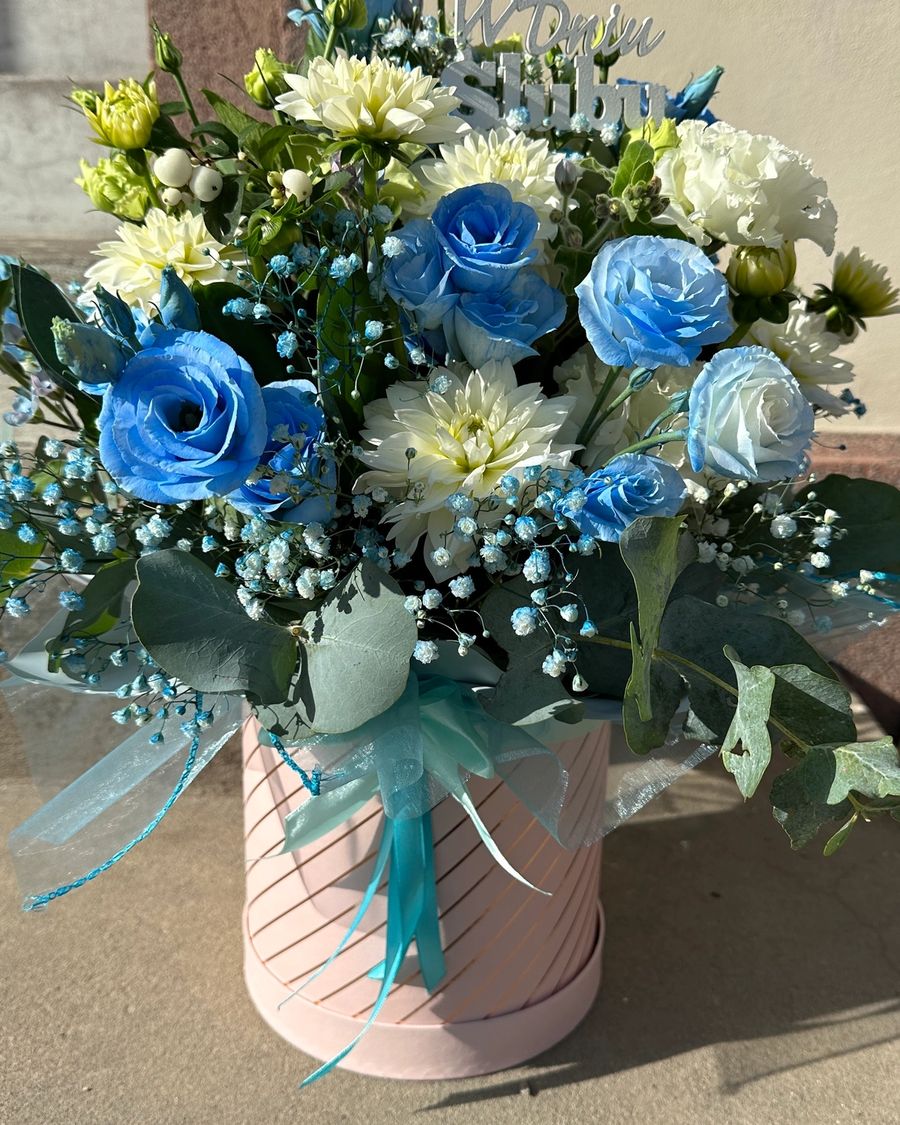 Delikatny flowerbox z niebieską eustomą oraz różnorodnymi kwiatami w kremowych odcieniach to subtelna kompozycja o eleganckim i świeżym charakterze.