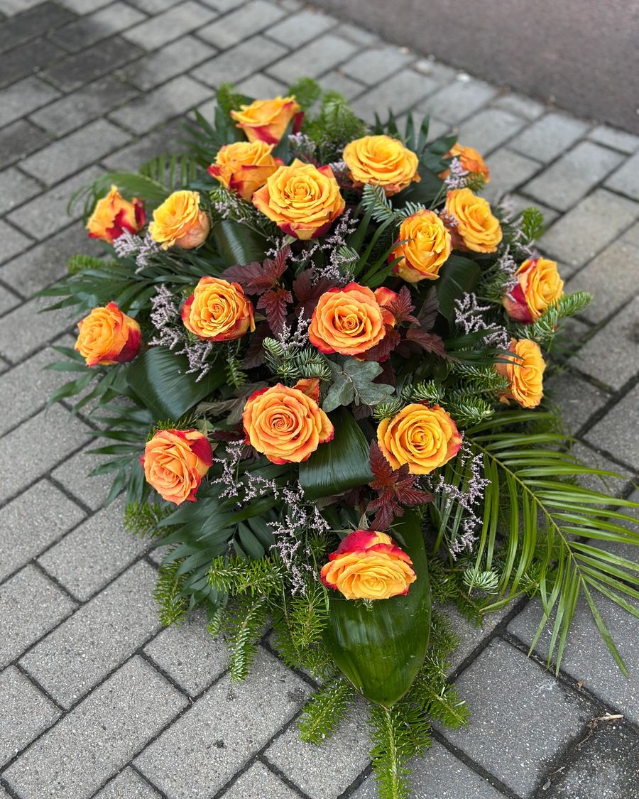 Wiązanka pogrzebowa w kształcie łezki z róż herbacianych, uzupełniona zielonymi dodatkami florystycznymi, ułożona na podkładzie z jodły i florecie z dostępem do wody ujęcie 2.