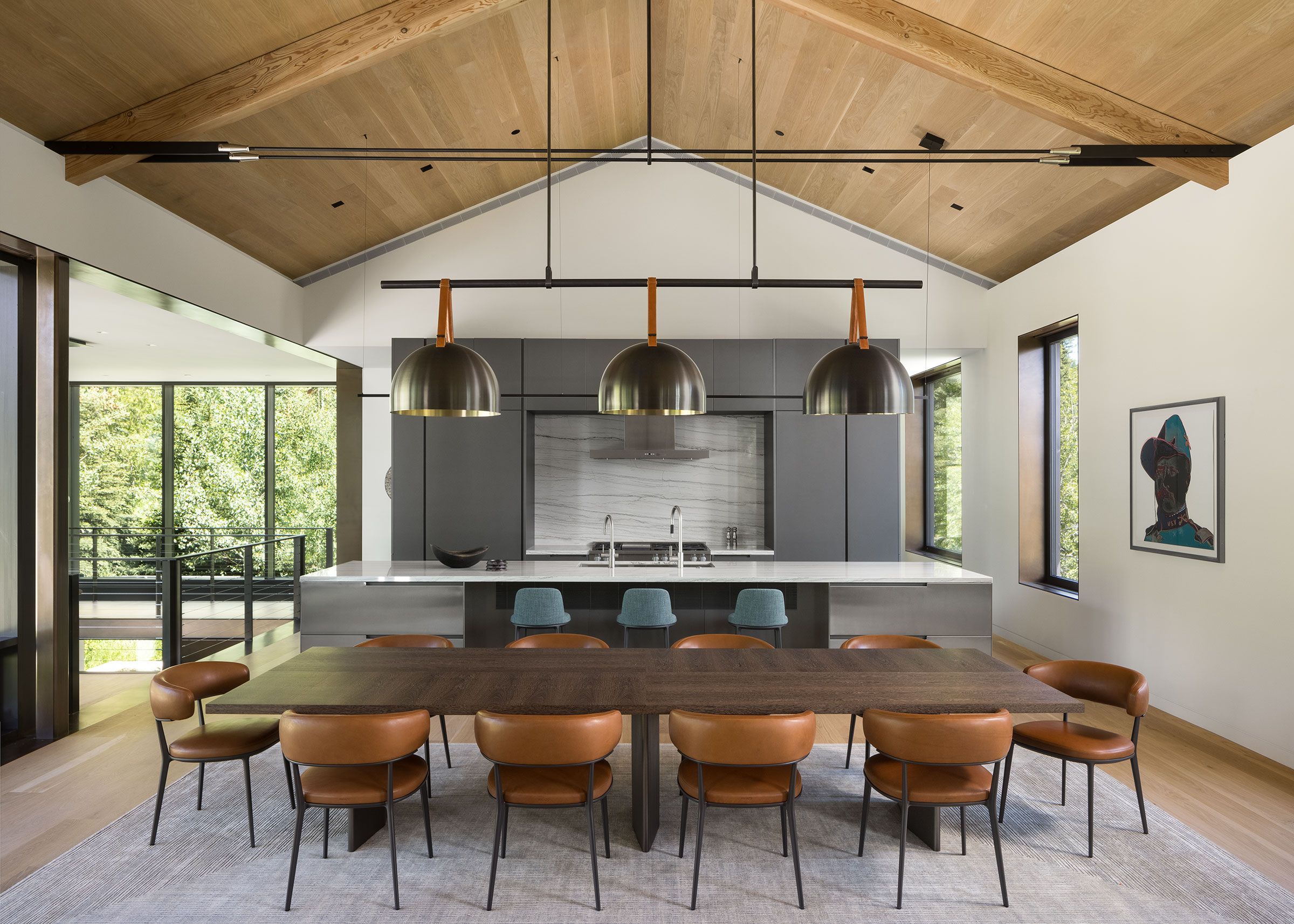 Modern open-concept dining room and kitchen under a high wood-paneled vaulted ceiling, featuring a long dark wood dining table with leather chairs and three large dome pendant lights.