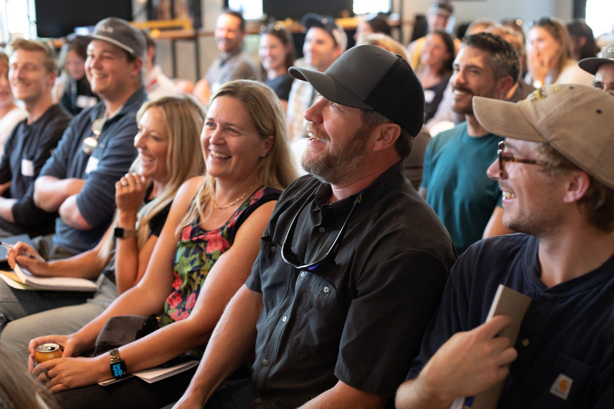 A cheerful and engaged audience of diverse adults laughing and smiling at an indoor event or presentation.