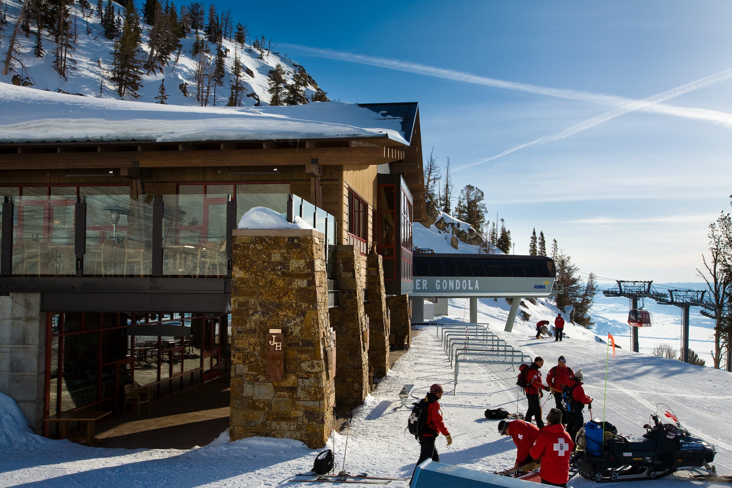 Jackson Hole ski patrol team with a snowmobile near the Pioneer Gondola station and a ski lodge on a sunny winter day.
