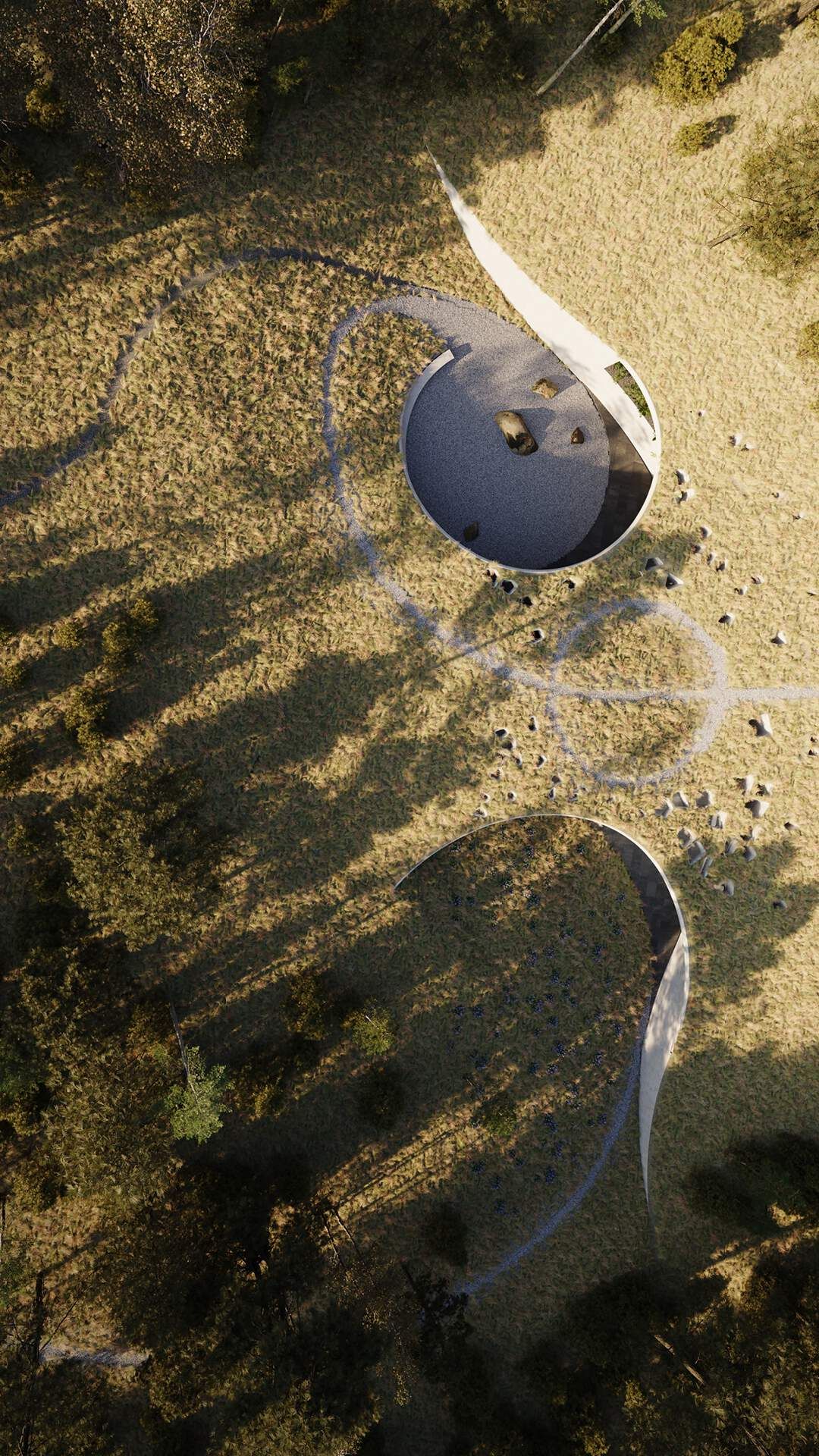 Aerial view of two minimalist circular architectural forms integrated into a golden grassy landscape with sparse trees. A winding path connects an open-air courtyard, featuring a gravel floor with large rocks and a sweeping white wall, to a second structure. Long tree shadows stretch across the sunlit field.