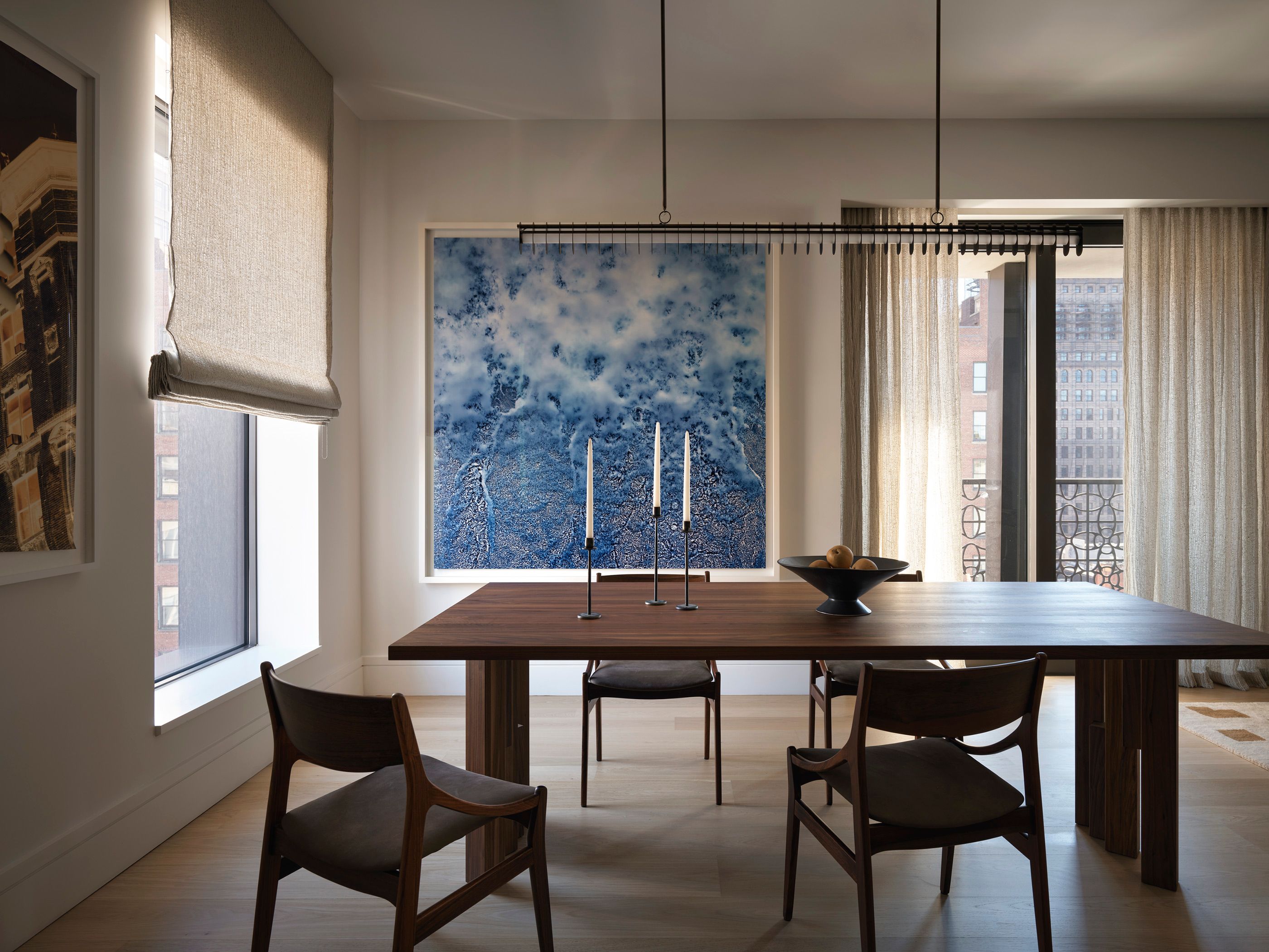 Modern minimalist dining room featuring a dark wood table, mid-century modern chairs, a linear black pendant light, and a large blue abstract wall art piece.