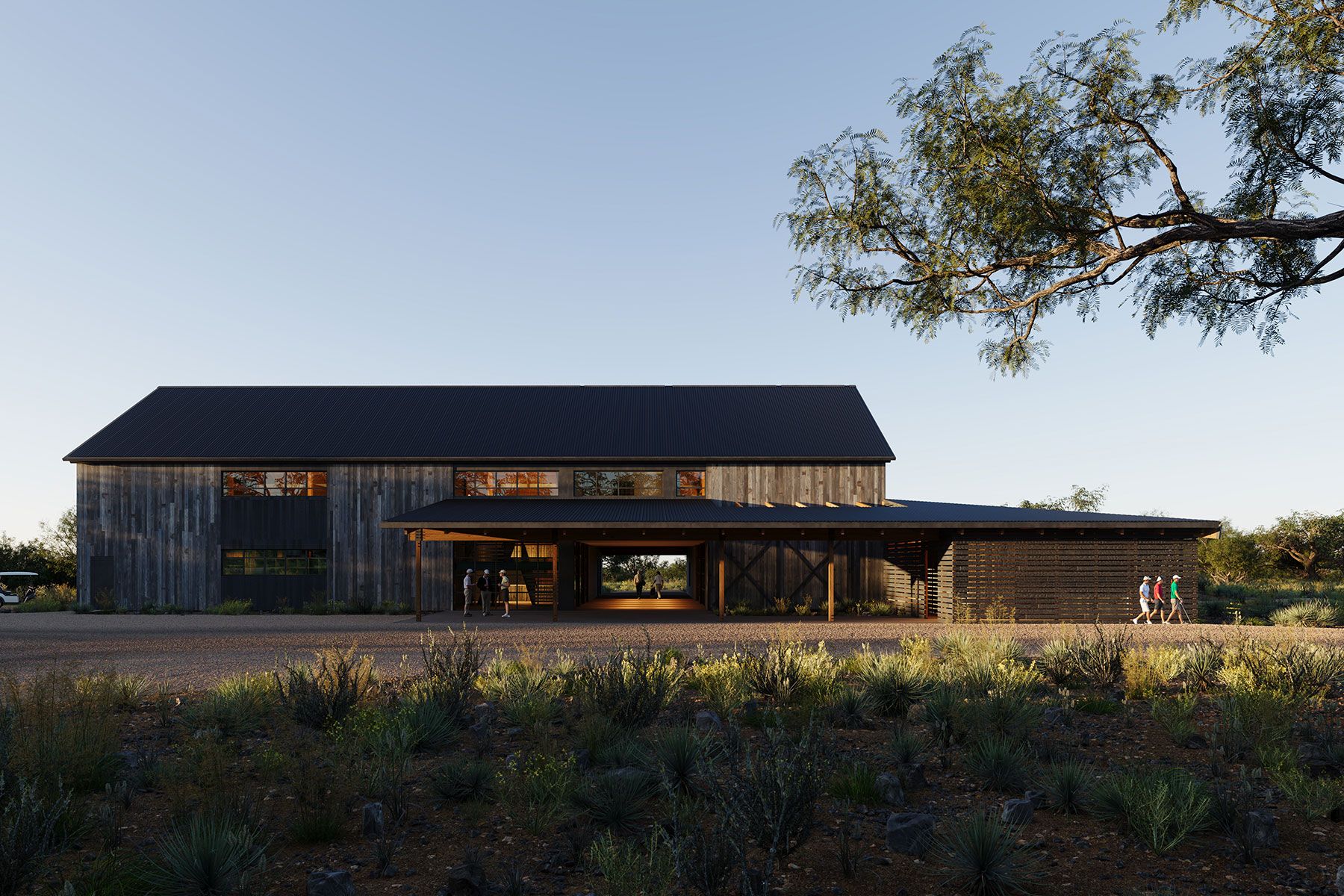 Modern rustic two-story wooden barn building with a low-slung dark metal roof, open breezeway, and surrounding desert landscaping at dusk.