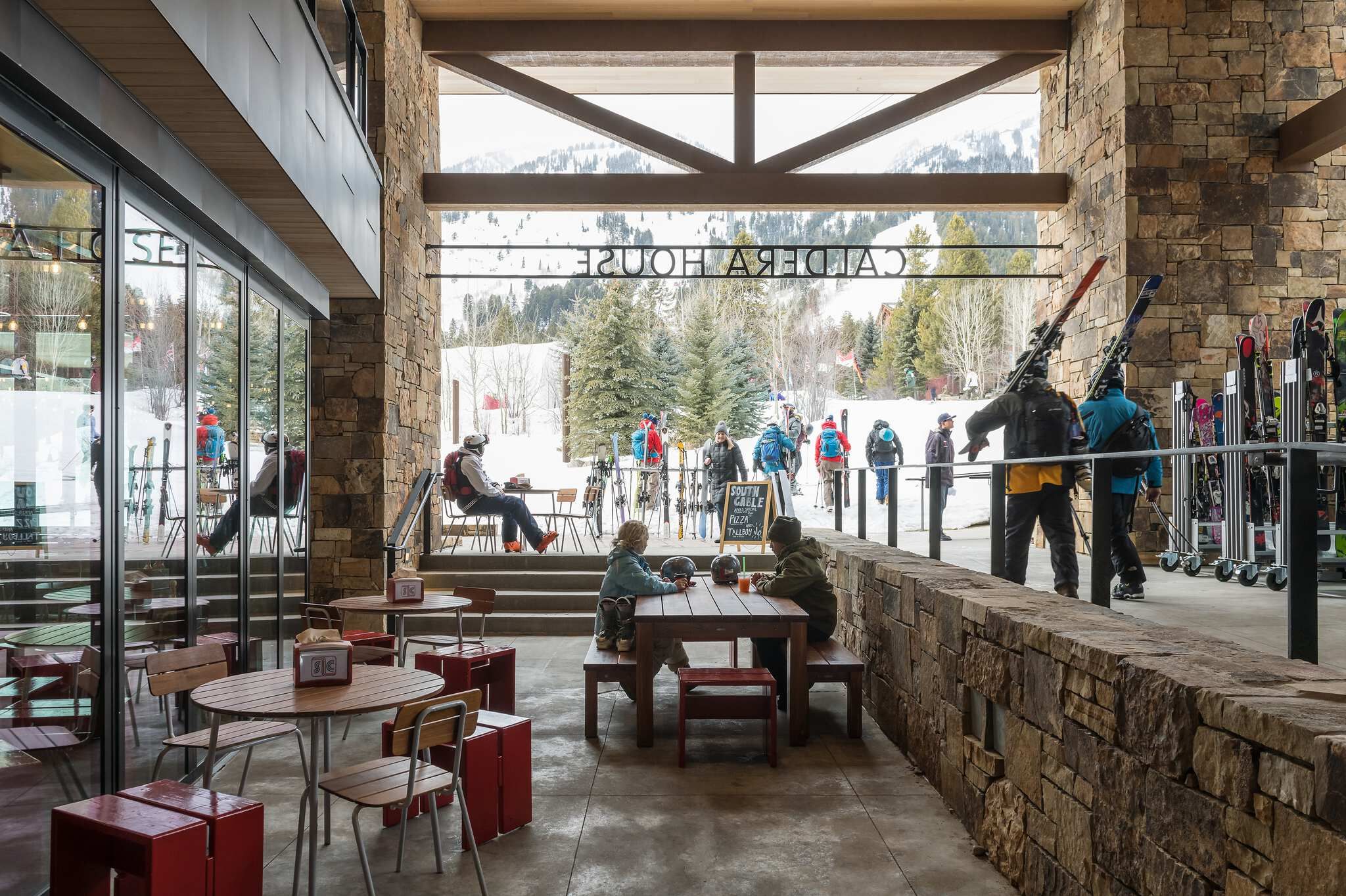 Caldera House ski lodge outdoor patio with skiers relaxing and gathering amidst rustic stone architecture and snowy mountains.