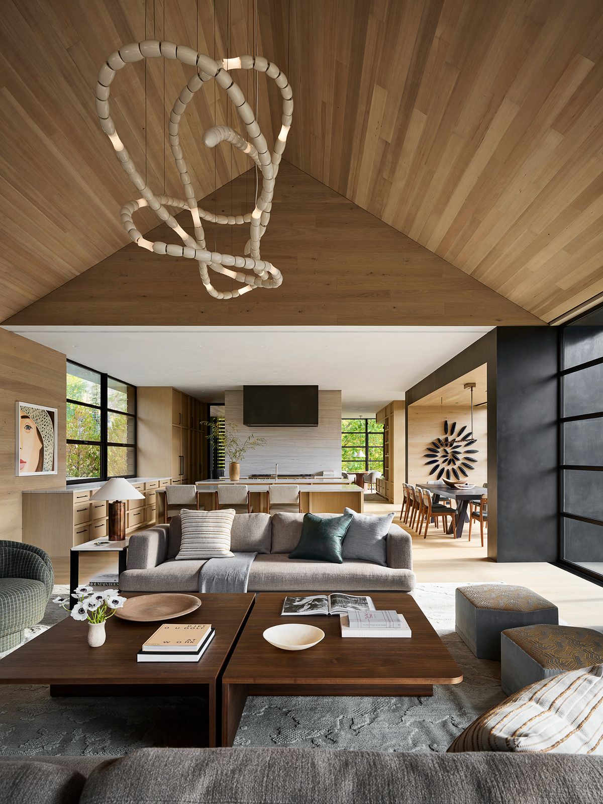 Spacious open-concept living room and kitchen with high vaulted wood ceilings, a unique sculptural chandelier, and contemporary furniture.