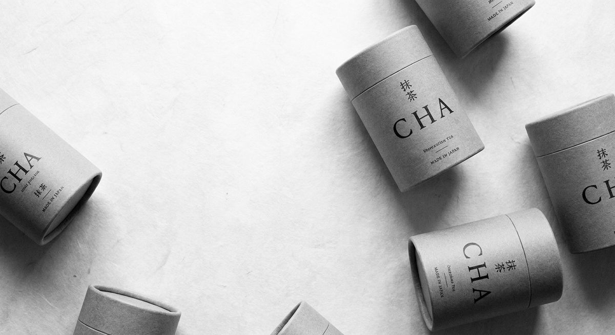 Kraft-paper tea tins with black ink typography arranged on warm off-white paper