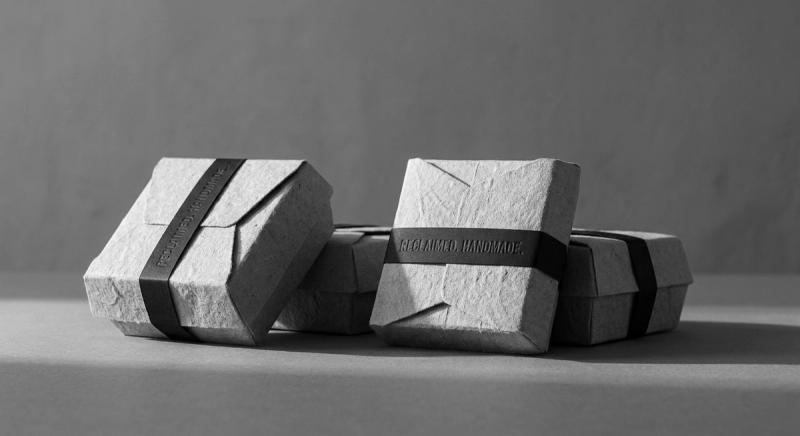 Folded cotton-paper cartons in raking light with a black letterpressed band
