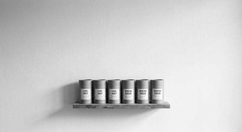 Row of kraft paper tea tins on a wooden shelf against a warm white wall