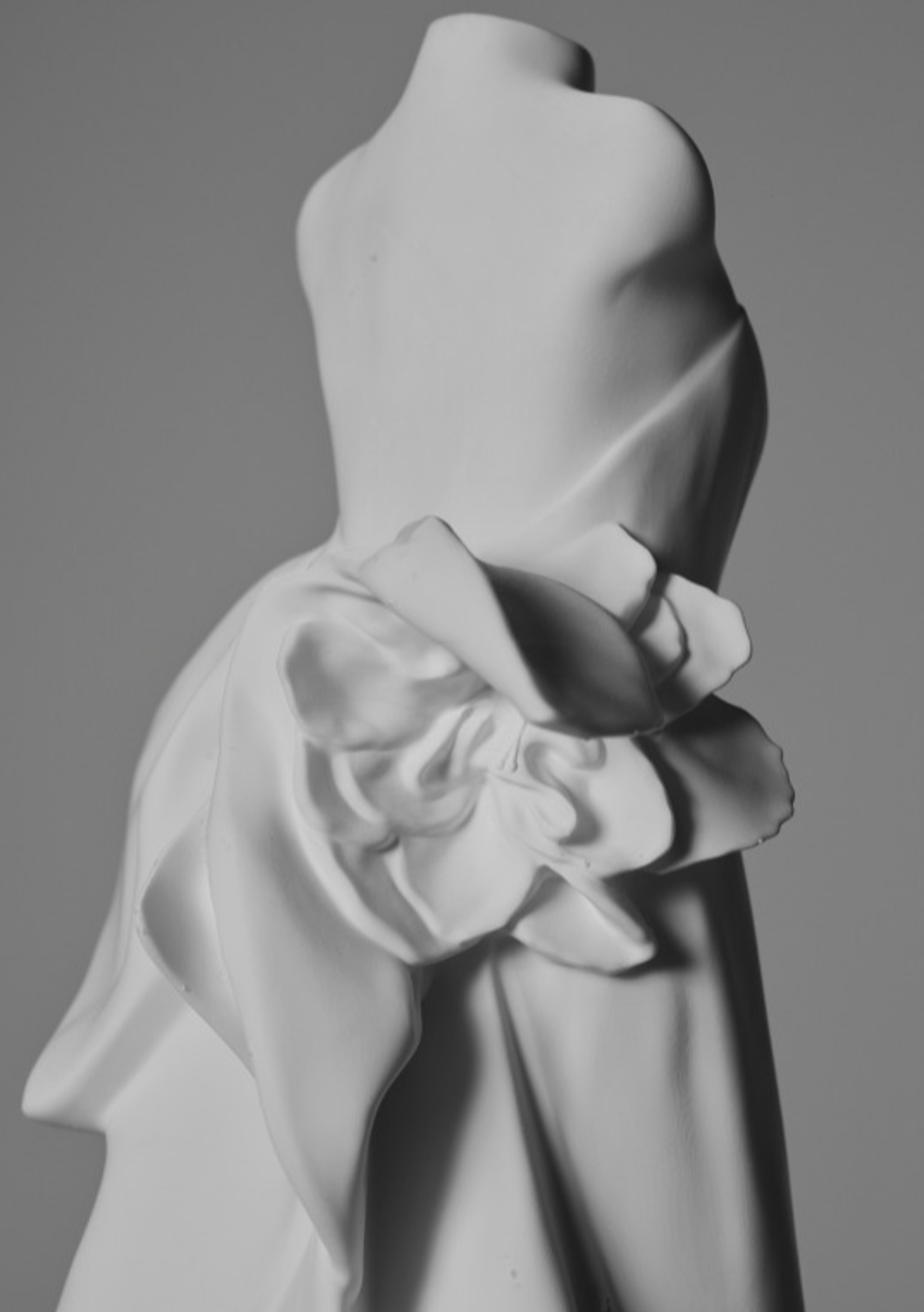 Close-up of a white wedding gown sculpture highlighting sculpted drapery, gathered fabric details, and surface texture.