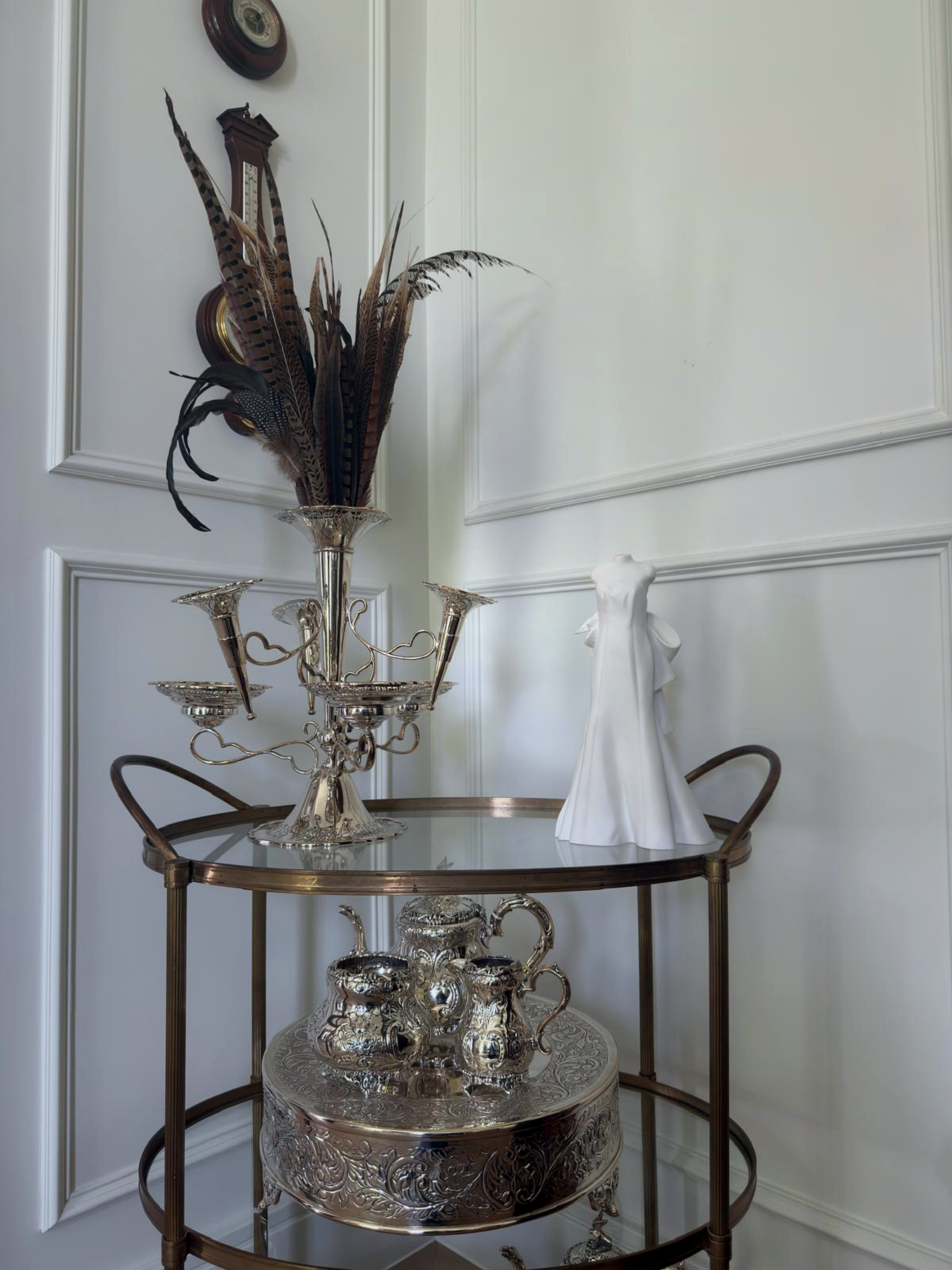 White wedding gown sculpture displayed on a silver bar cart beside decorative glassware in a residential interior.