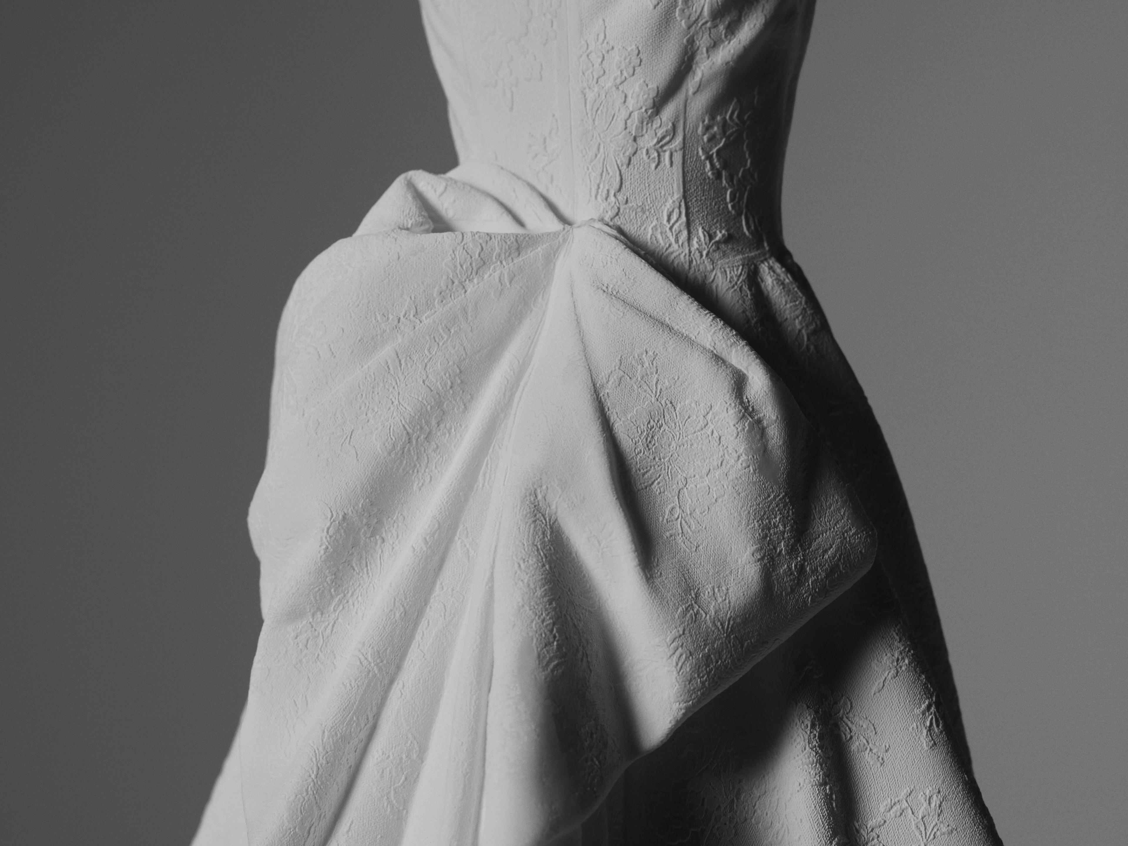 Close-up of a white wedding gown sculpture highlighting draped fabric folds, gathered detailing, and textured surface craftsmanship.