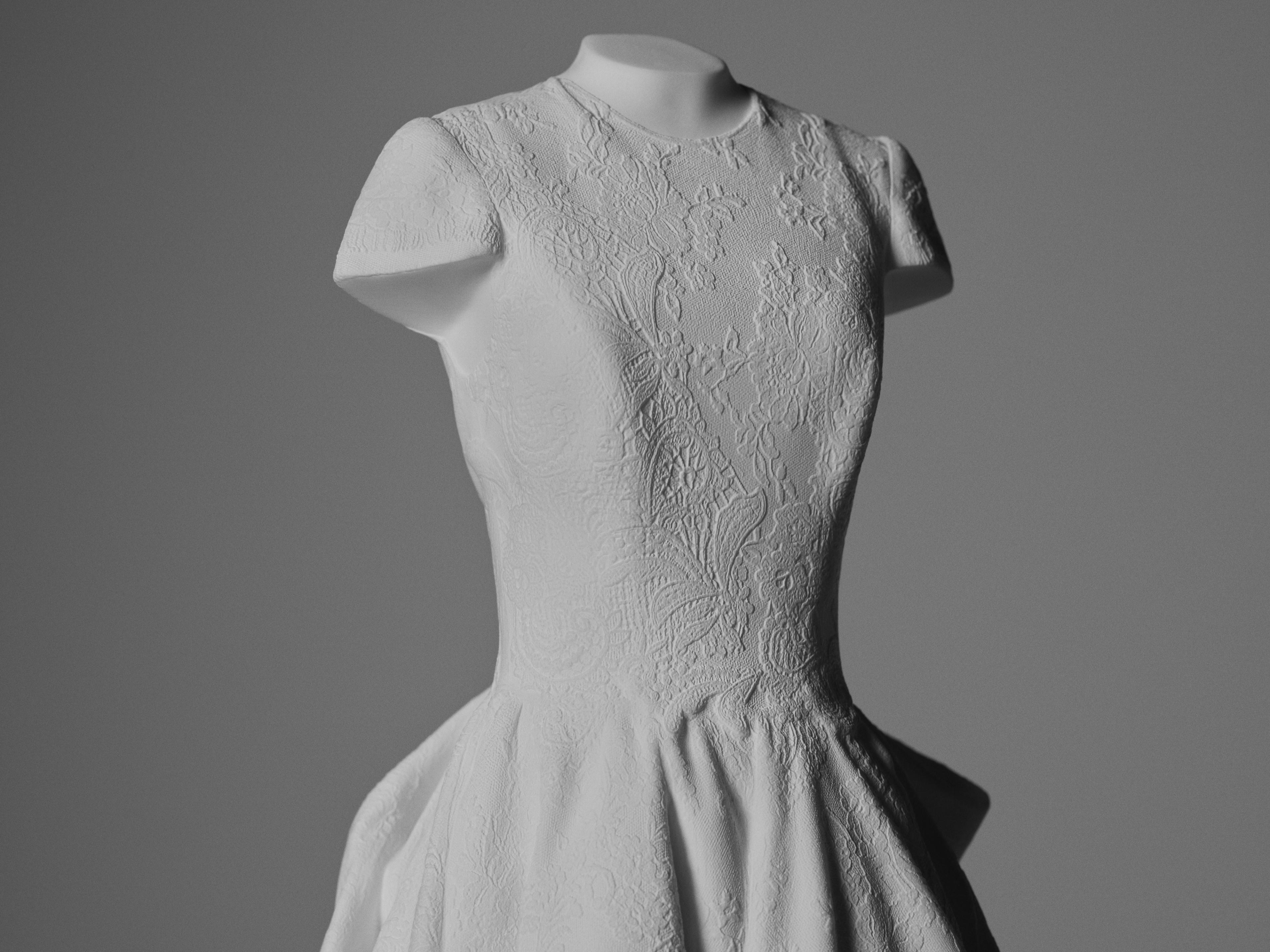 Close-up of a white wedding gown sculpture highlighting lace detailing, tailored seams, and sculptural form.