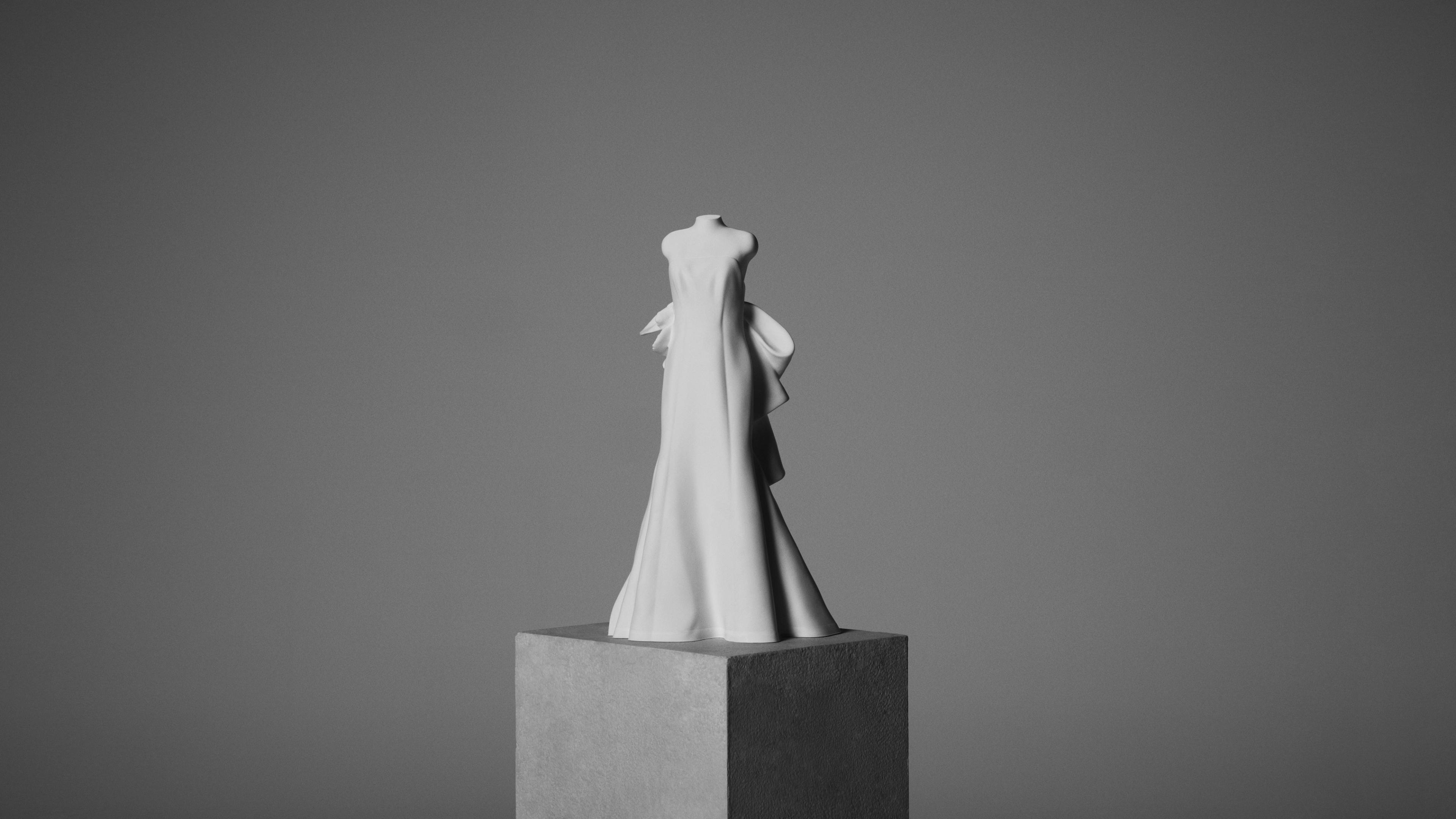 White wedding gown sculpture displayed on a pedestal against a neutral gray background.