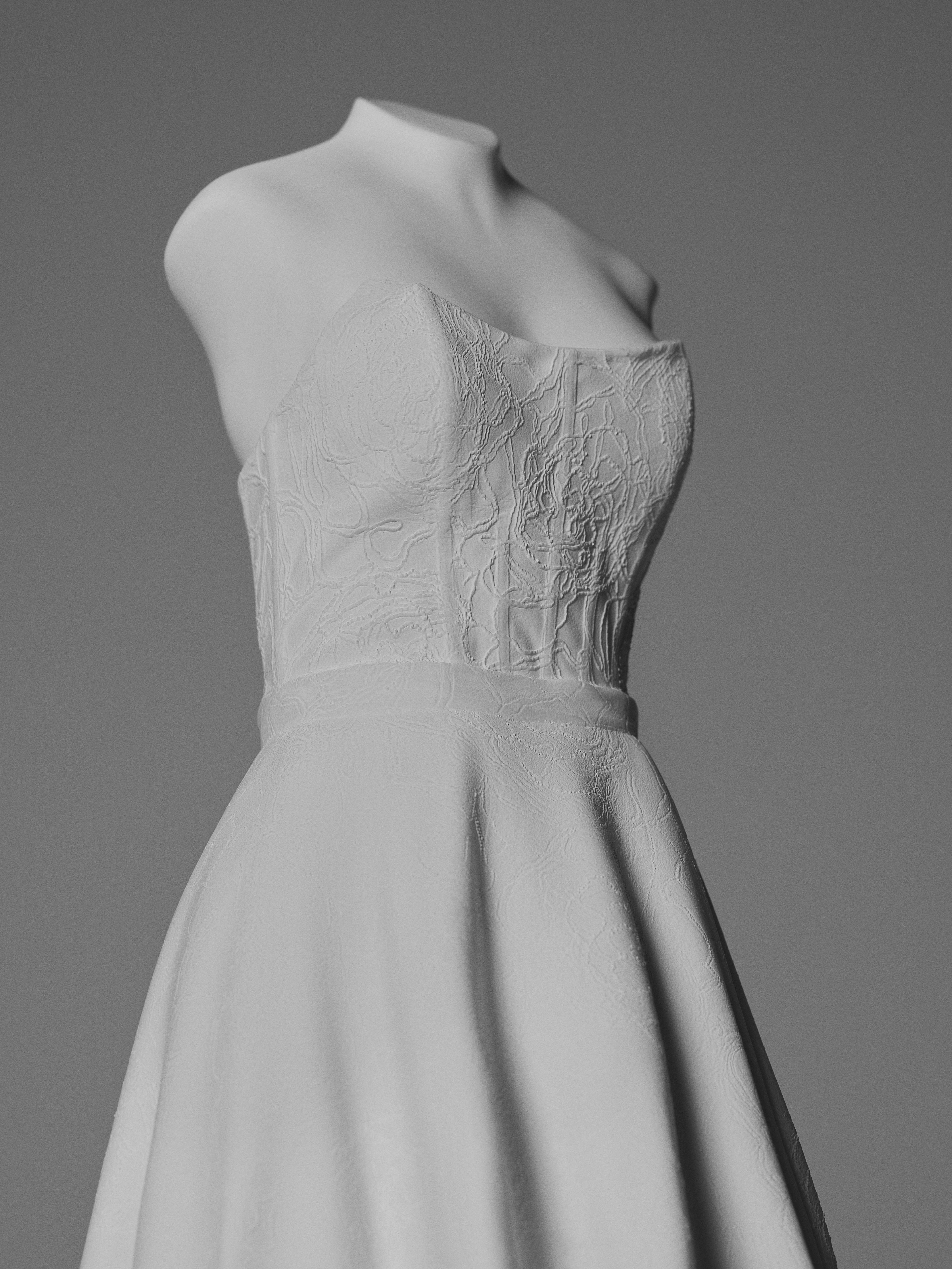 Close-up of a white wedding gown sculpture showing a fitted bodice, textured fabric detailing, and flowing skirt.